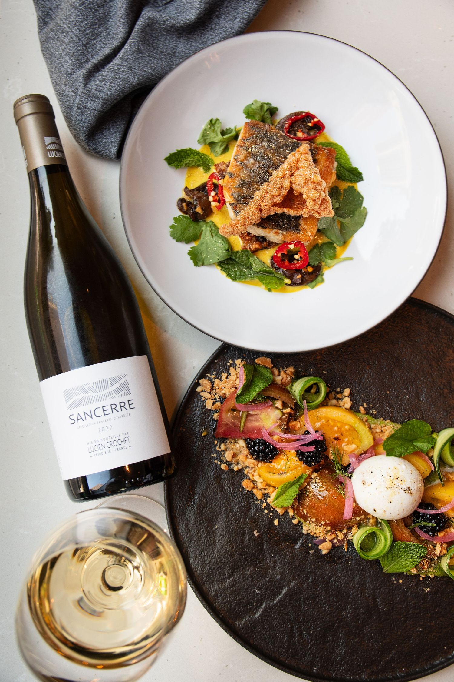 Elegantly plated dishes with wine pairings served on dark stone plates.