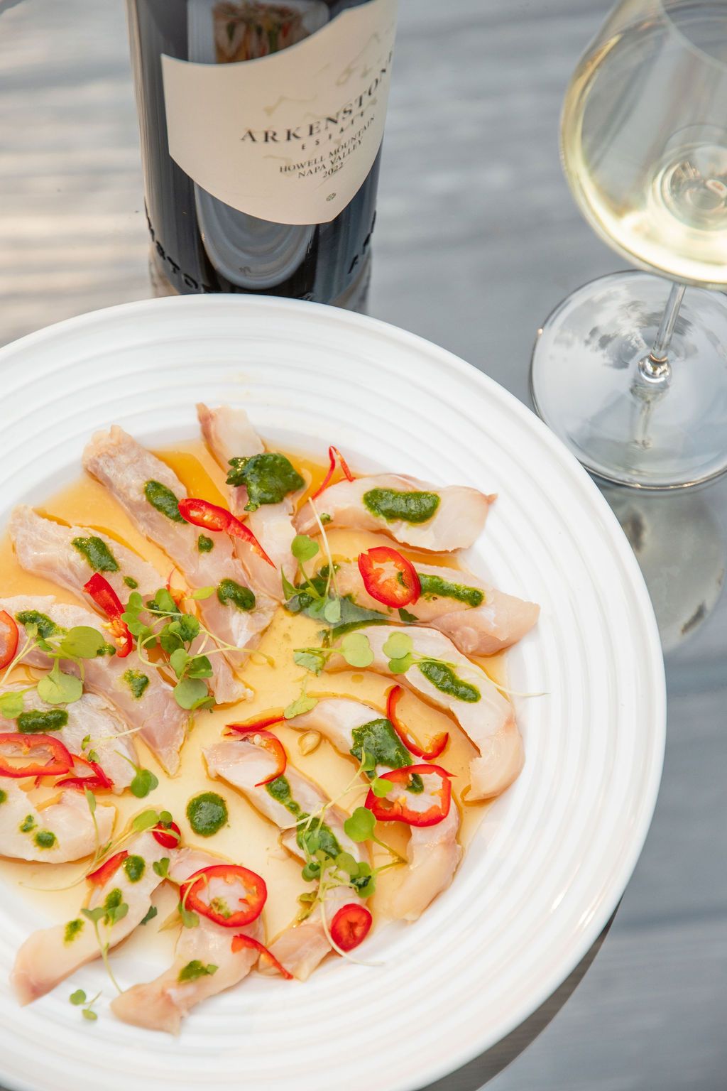Fresh hamachi crudo garnished with sliced chilis and herbs on white plates.