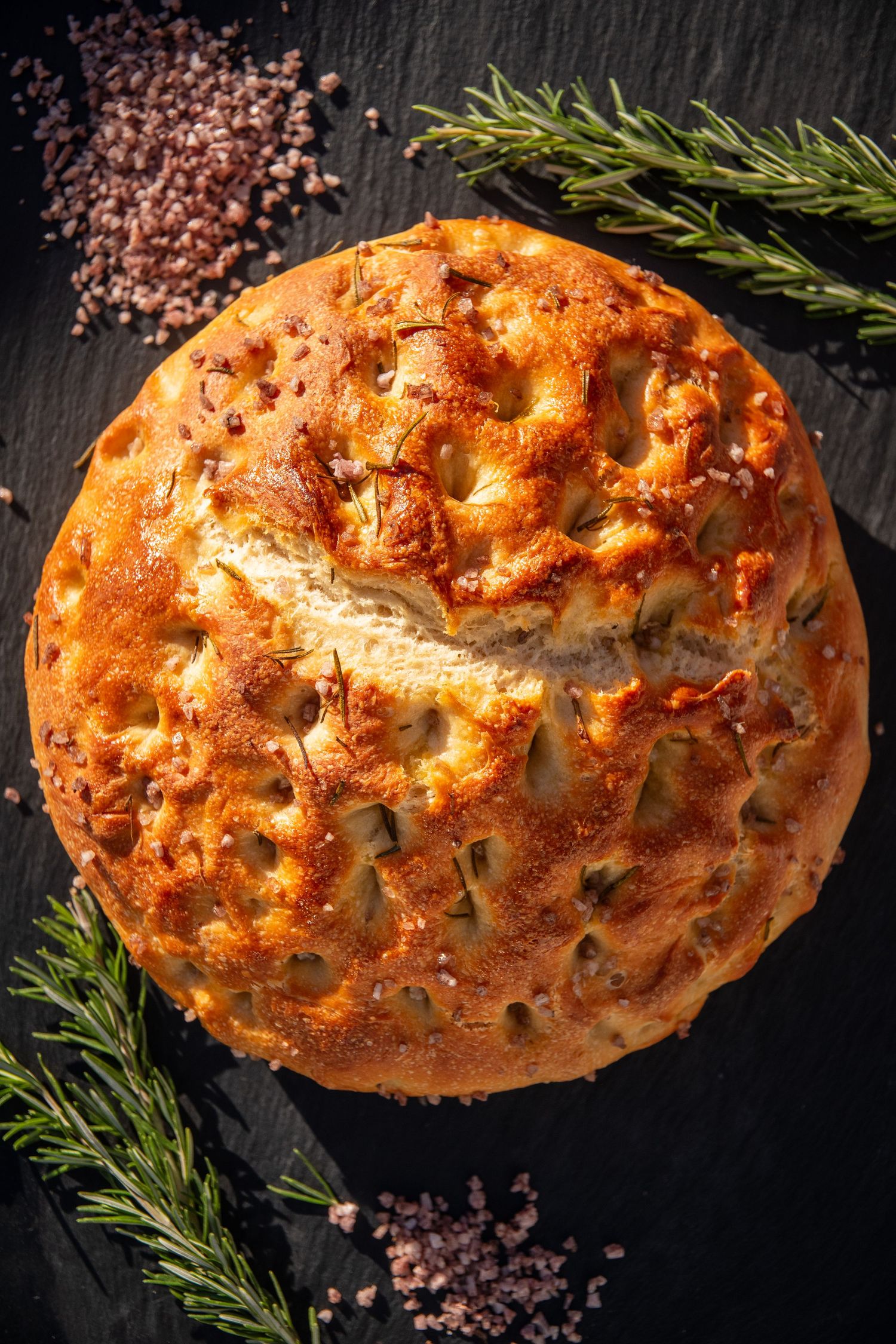 Artisanal bread loaf with golden crust and decorative scoring pattern on dark slate surface.