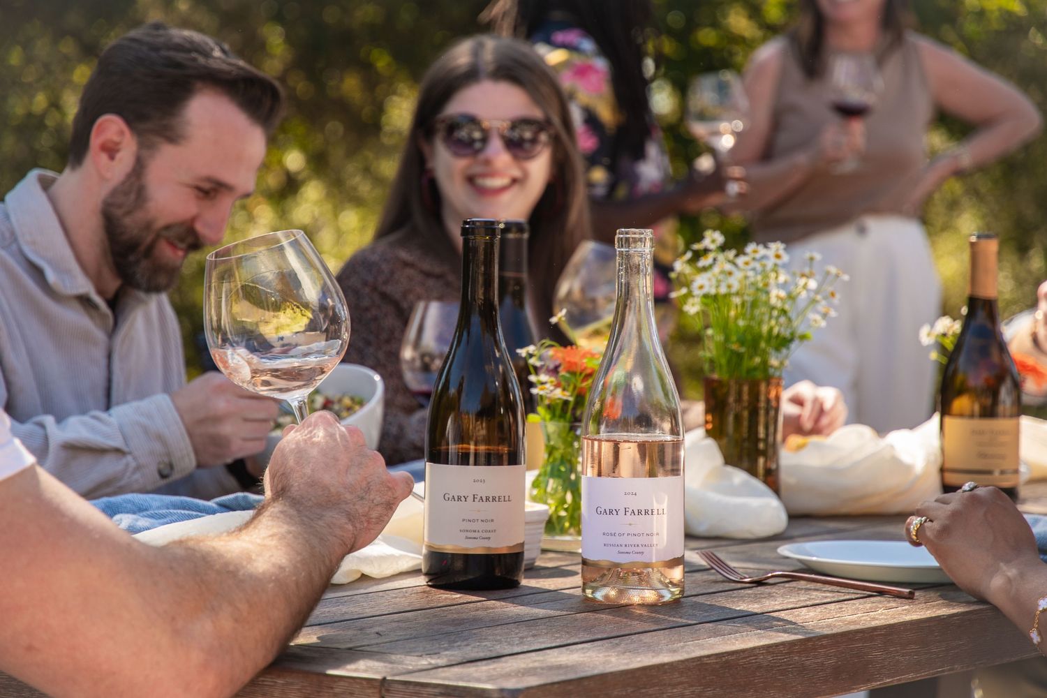 Friends gathered outdoors for wine tasting in natural setting.