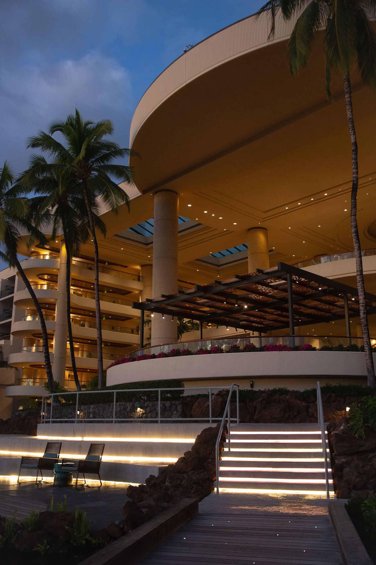 Modern resort entrance with curved architecture and palm trees at dusk.