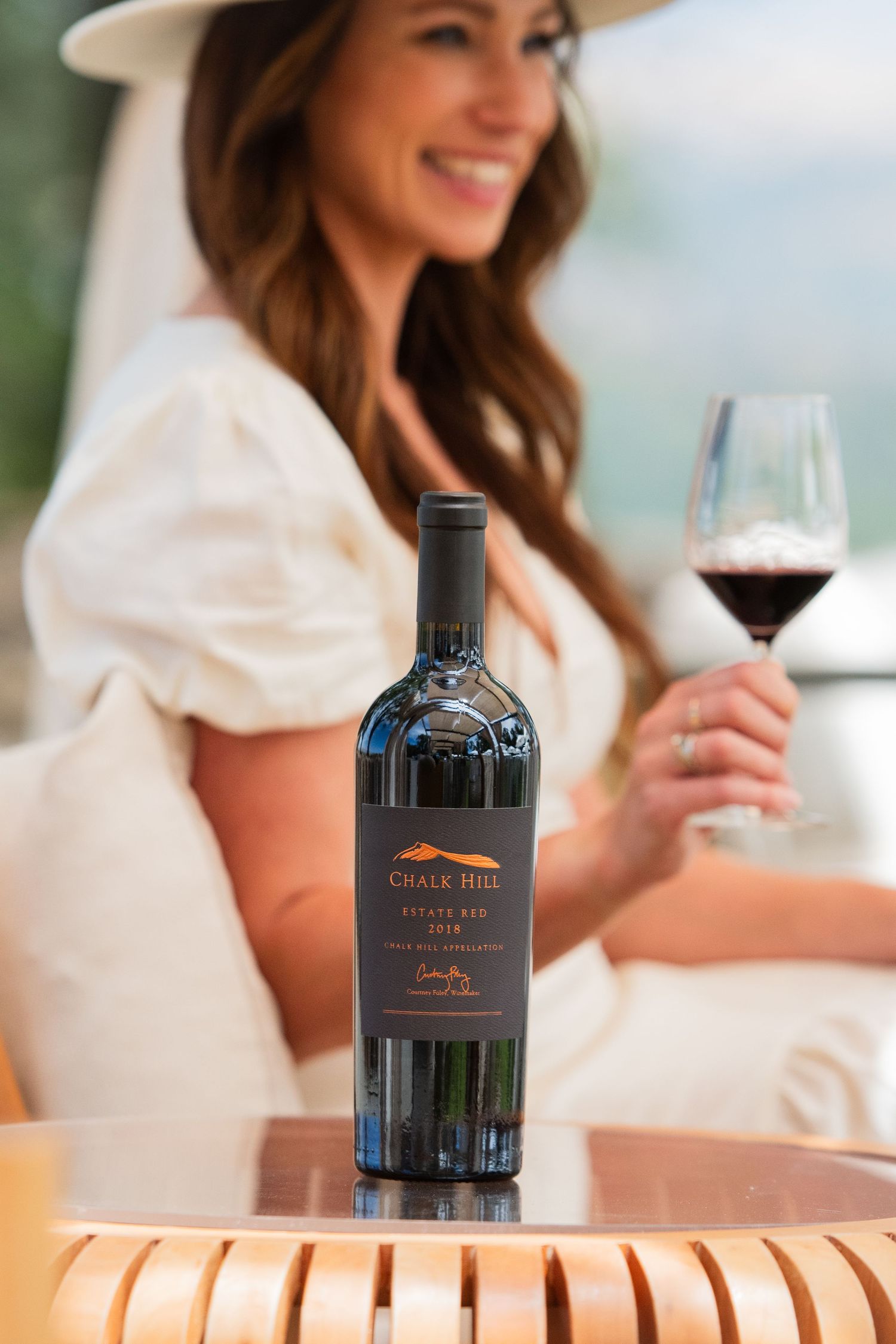 Elegant wine bottle and glass displayed on wooden deck railing with blurred background.