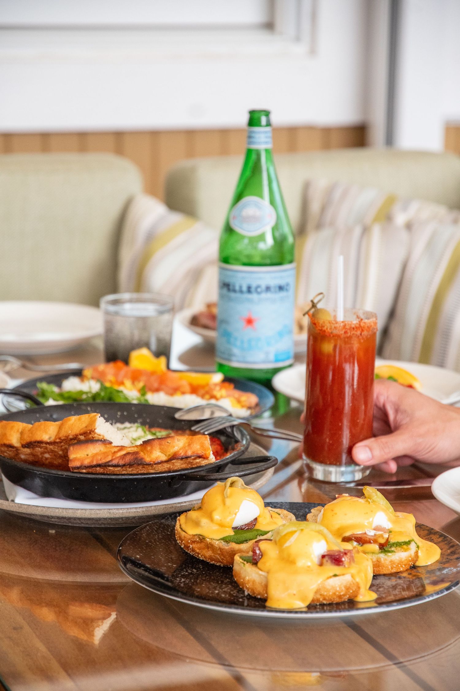 Brunch dishes including eggs benedict with hollandaise sauce and San Pellegrino sparkling water on a wooden table.