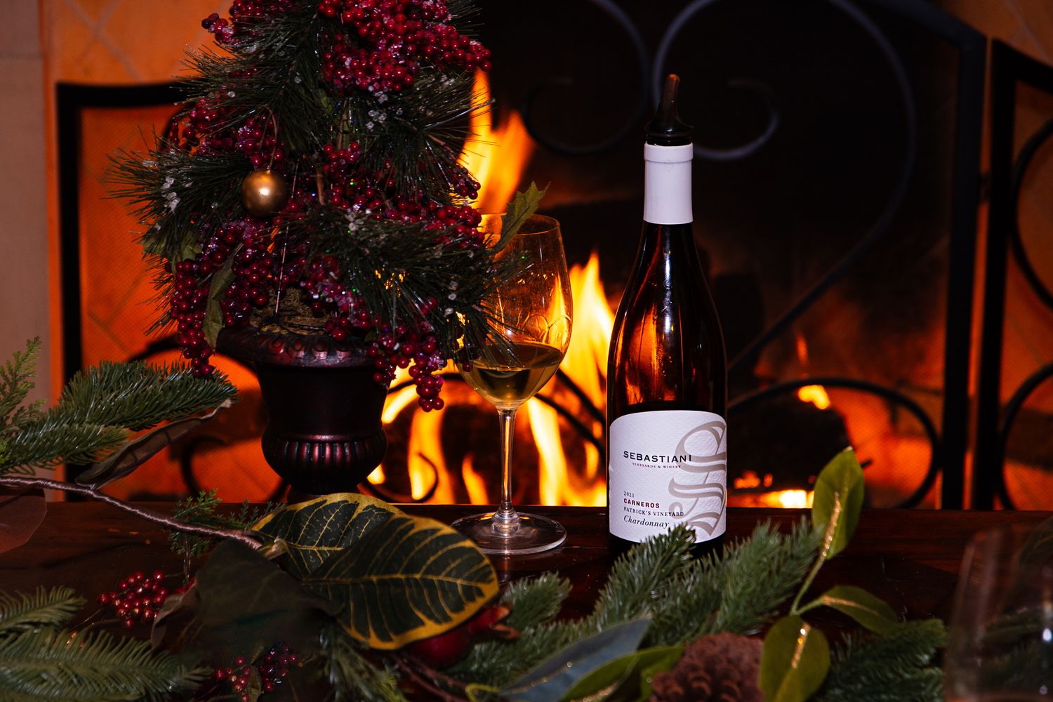 Cozy fireplace scene with red berries, wine bottles and holiday decorations creating a warm ambiance.