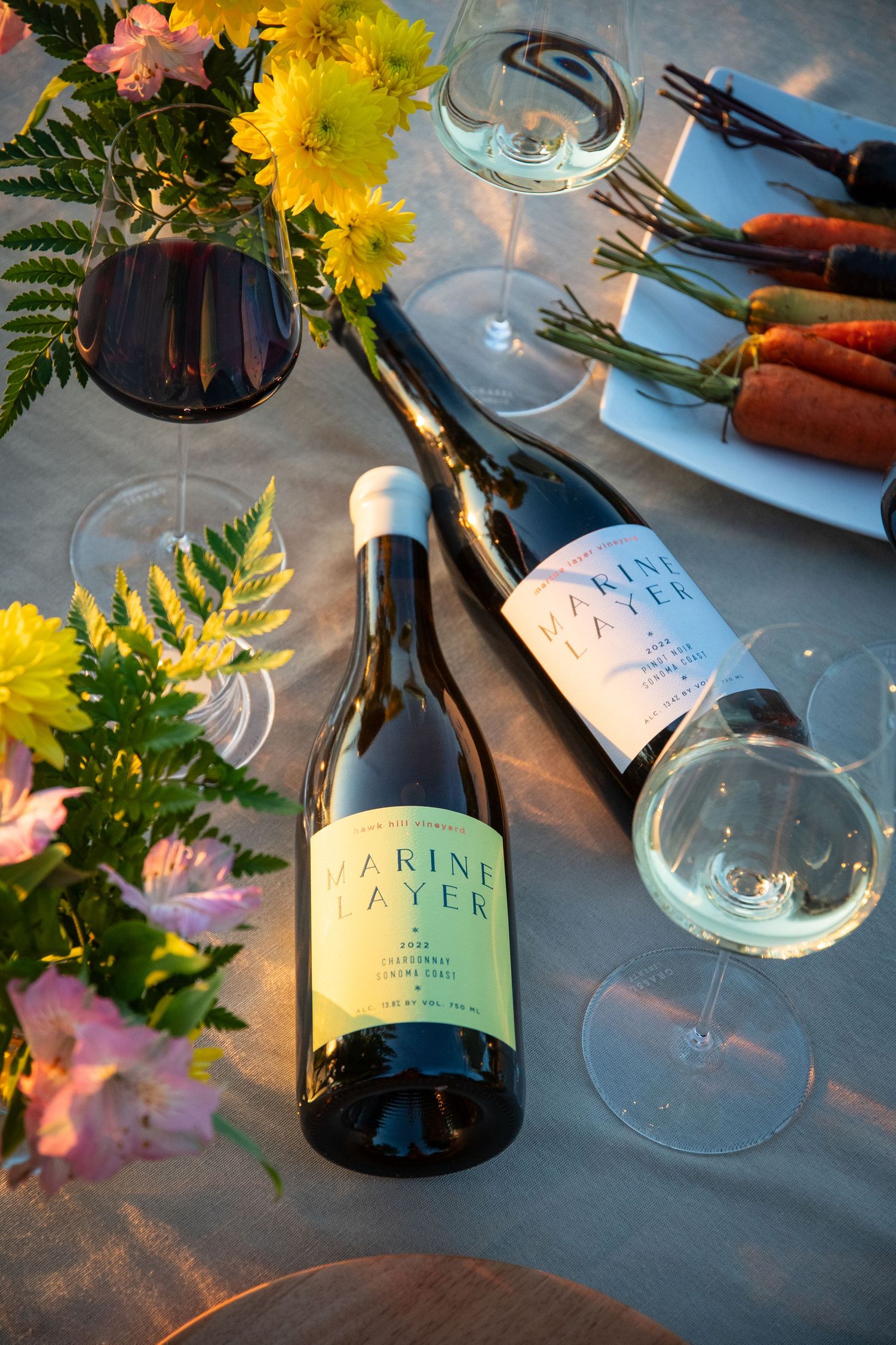 Wine bottles and glasses arranged with yellow flowers and greenery on a blue surface.