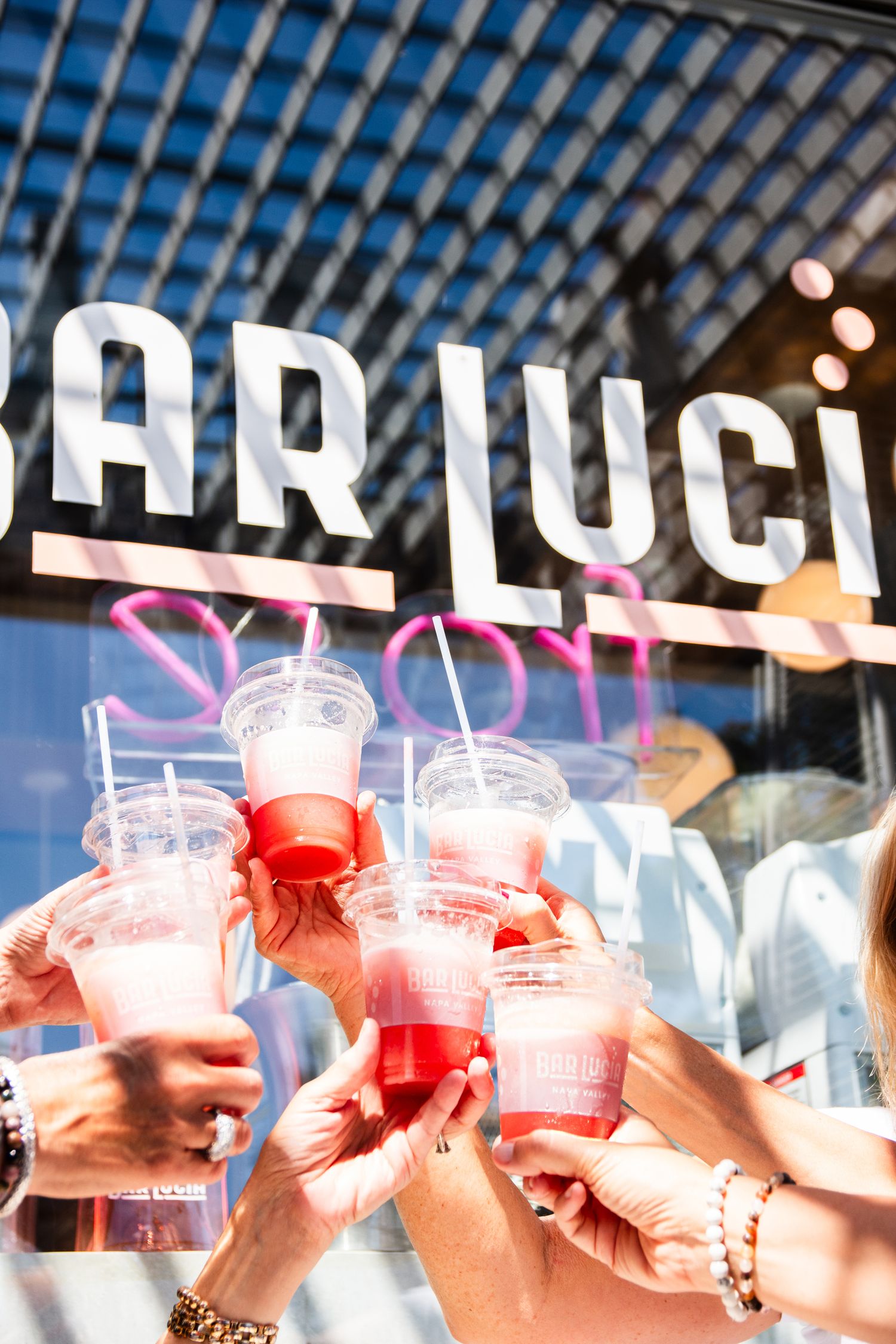 Group toasting with pink cocktails against Bar Lucia signage.