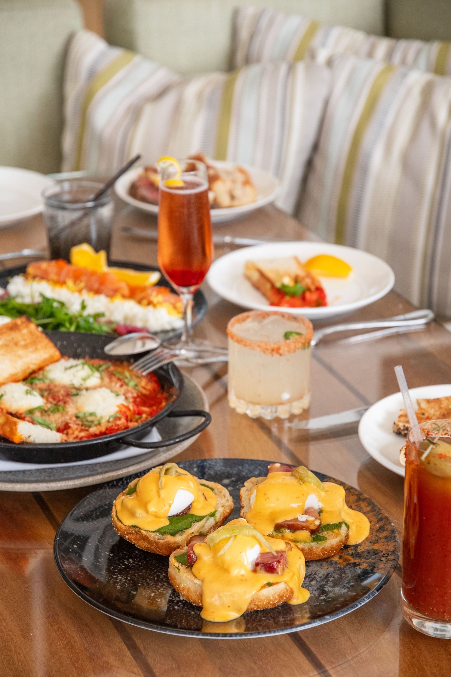 Elegant brunch table setting with eggs benedict, cocktails and various breakfast dishes.