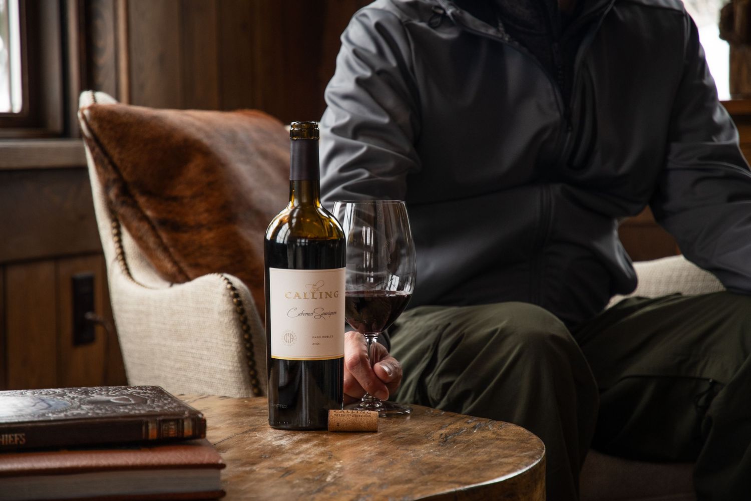 Bottle of red wine and glass on wooden table in cozy cabin setting.