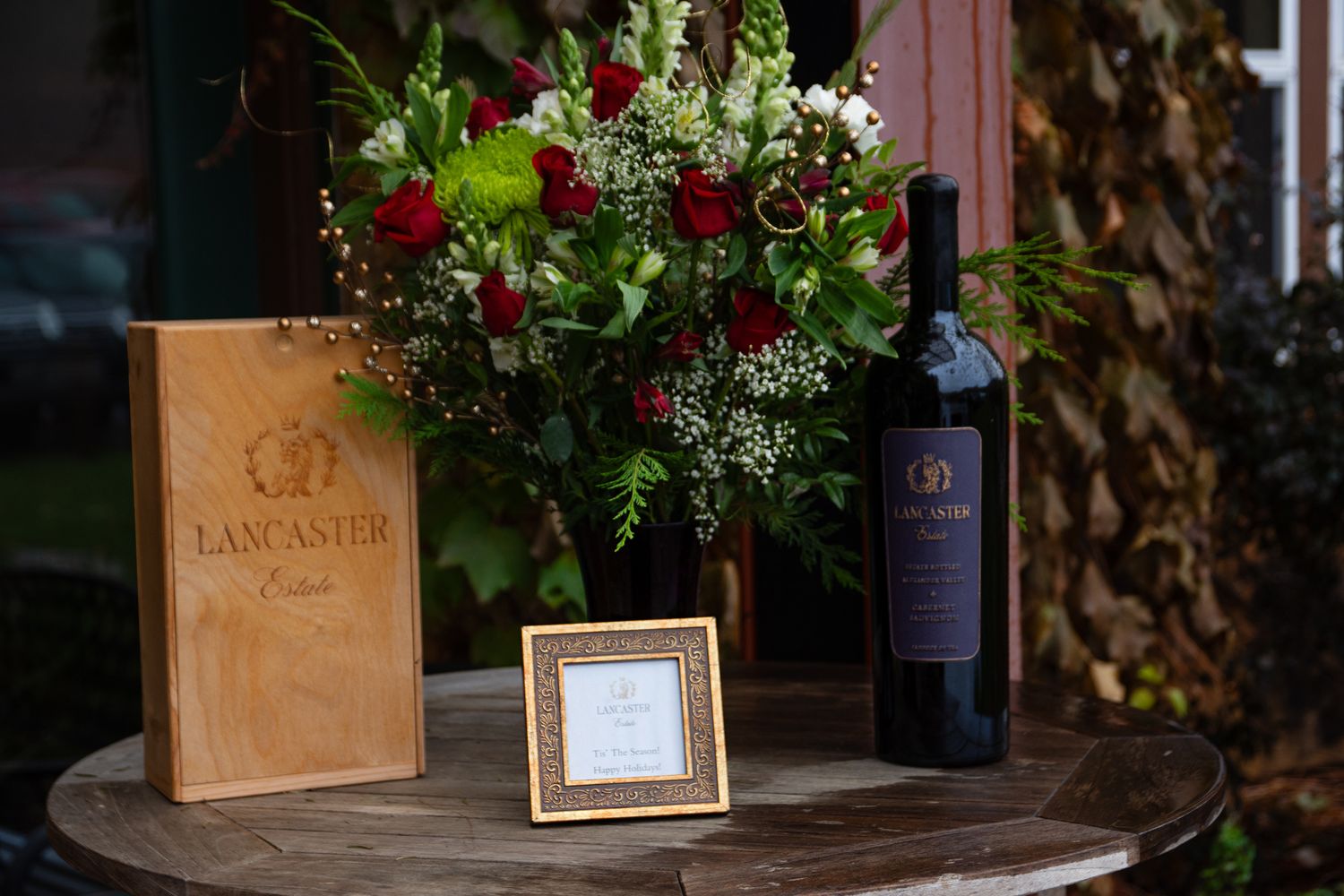 Wine bottle and wooden box display with fresh floral arrangement on rustic table.