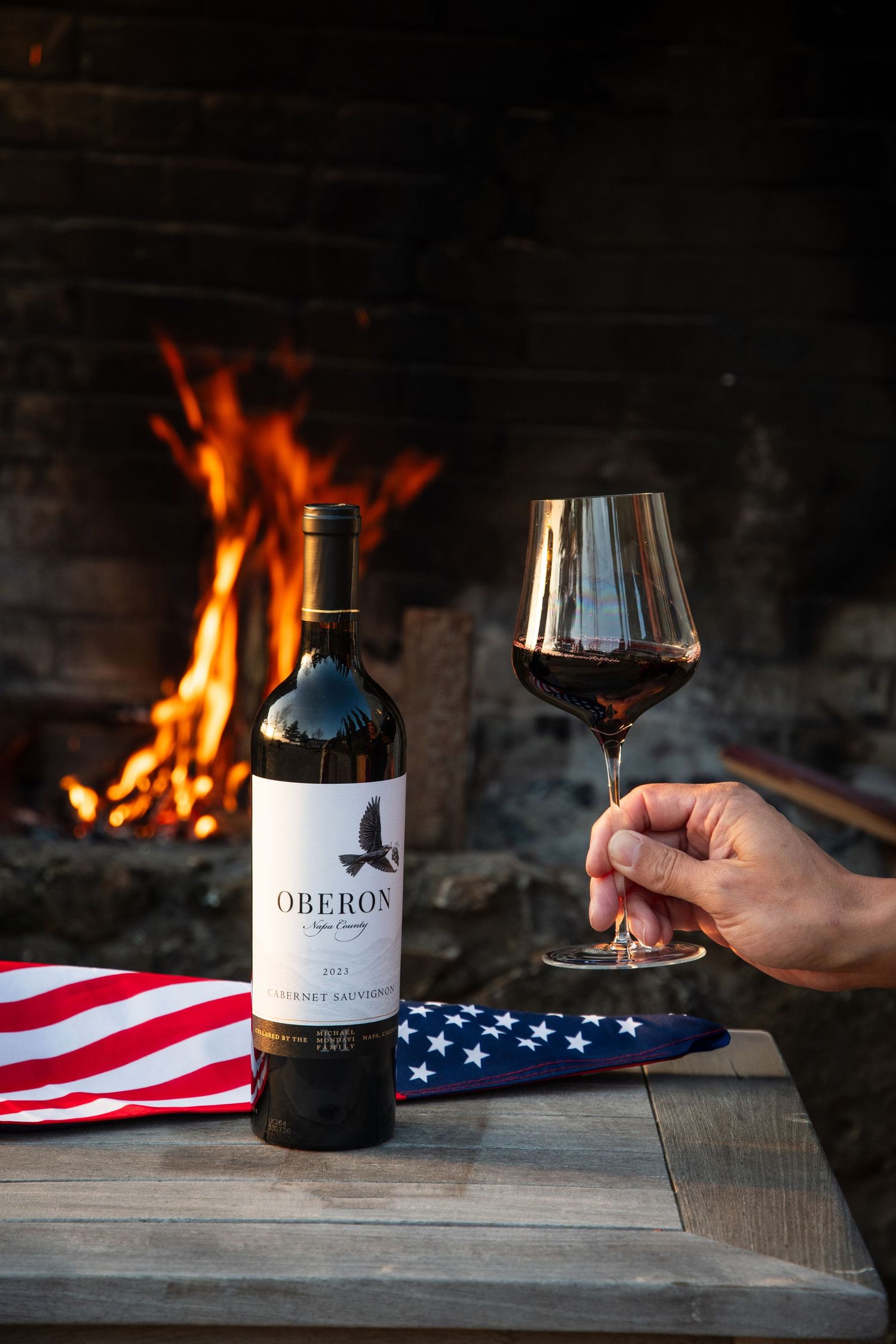Wine glass and bottle beside American flag with cozy fireplace in background.