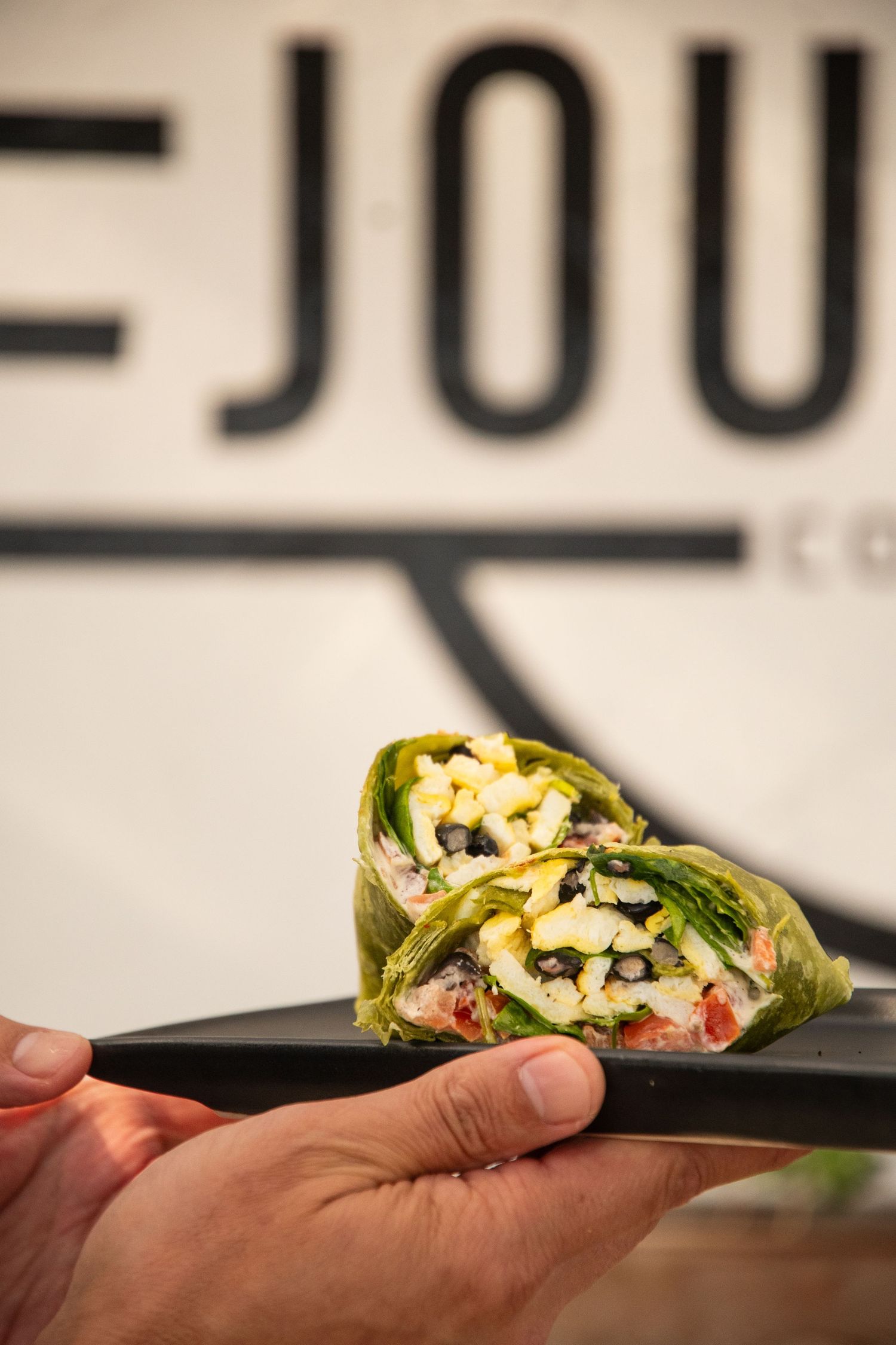 Lettuce wrap filled with fresh ingredients held over dark plate at Journey Coffee Co.