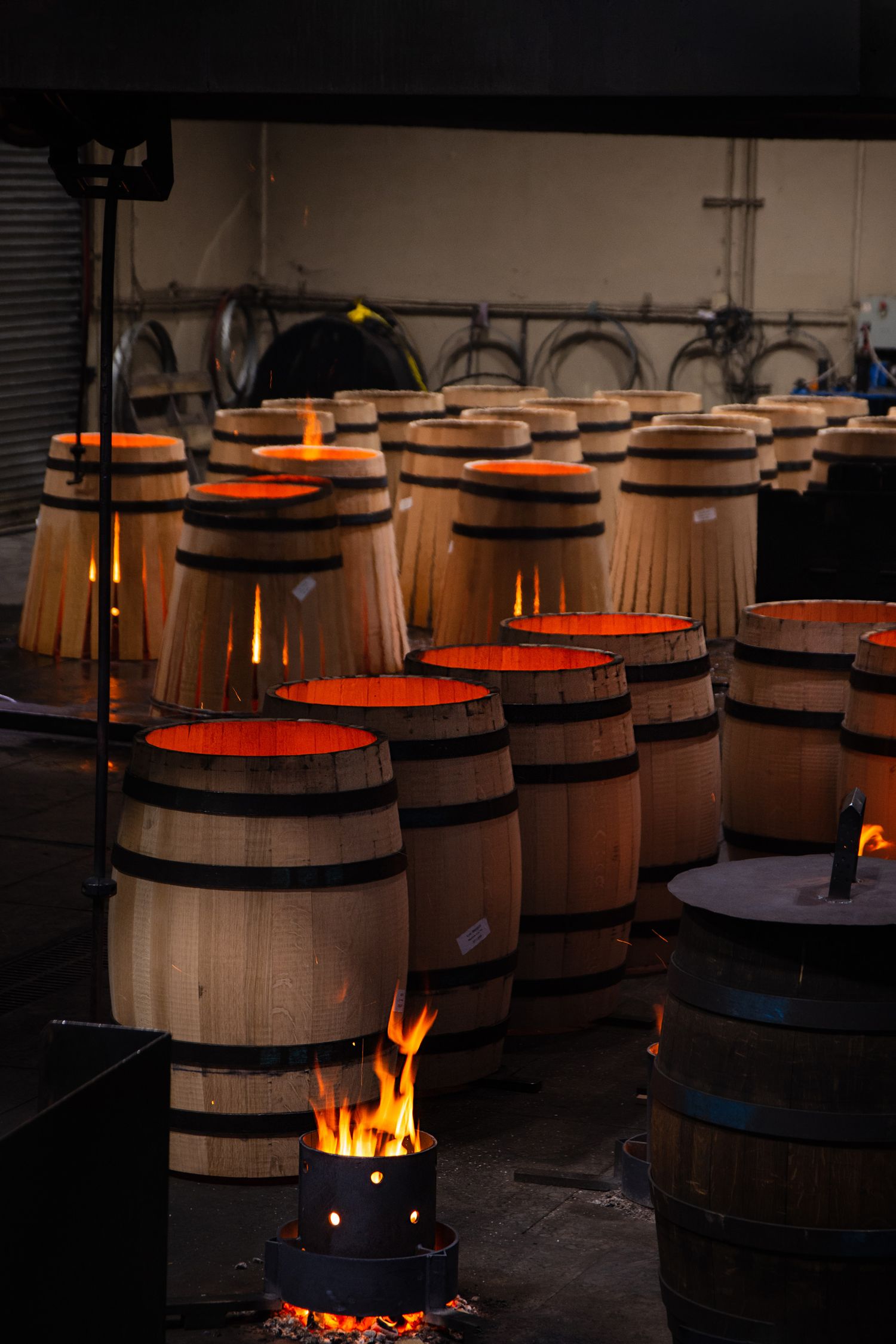 Wooden wine barrels being charred with flames in a dark cellar.