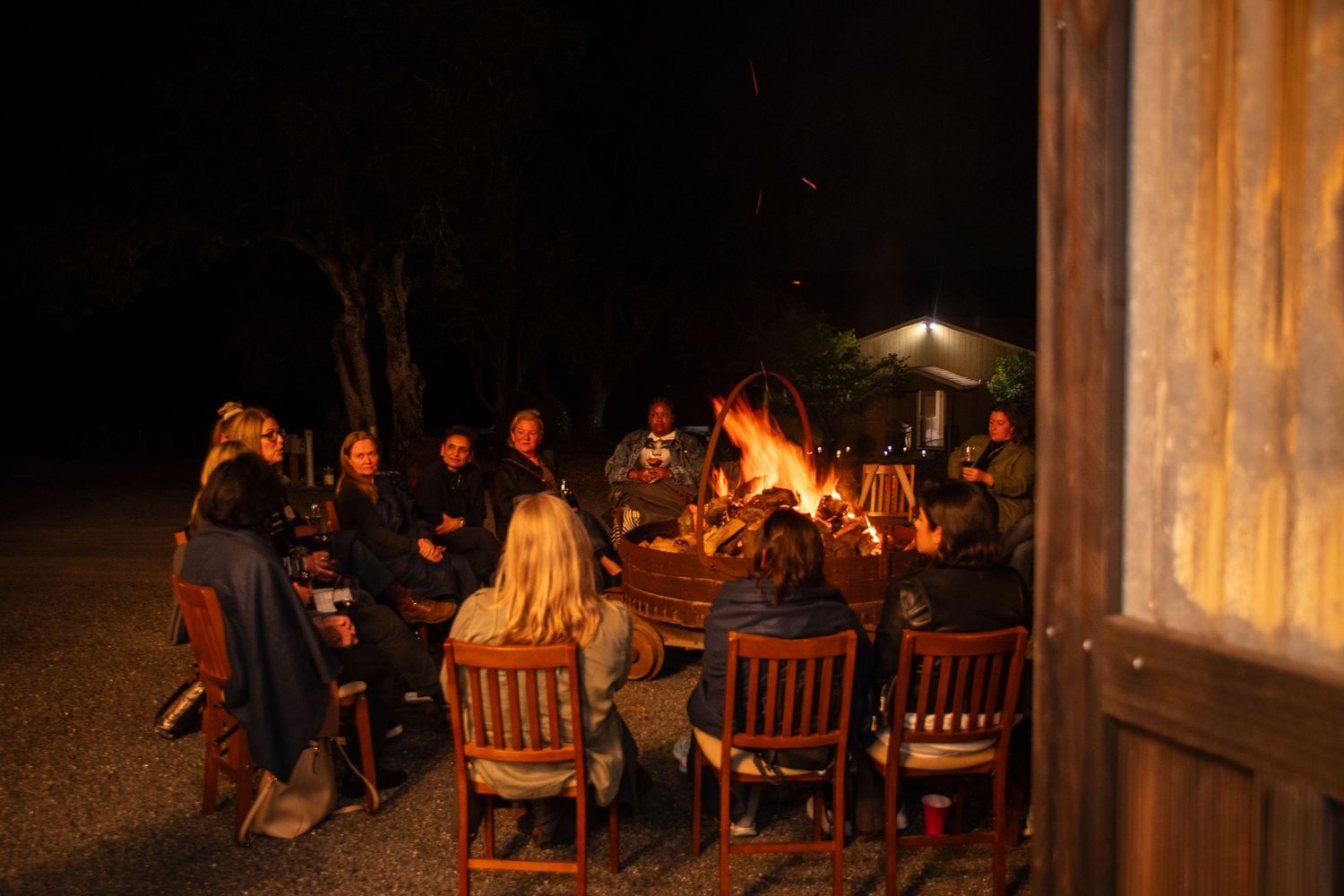 Evening gathering around tables and a fire pit in a rustic outdoor setting.