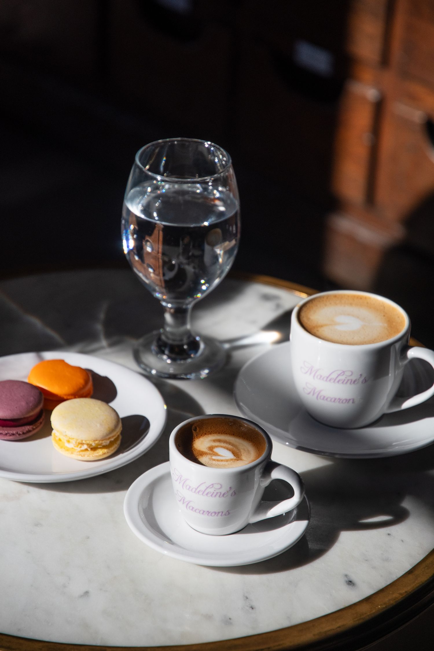 Coffee cups and colorful macarons arranged on a marble surface in natural lighting.