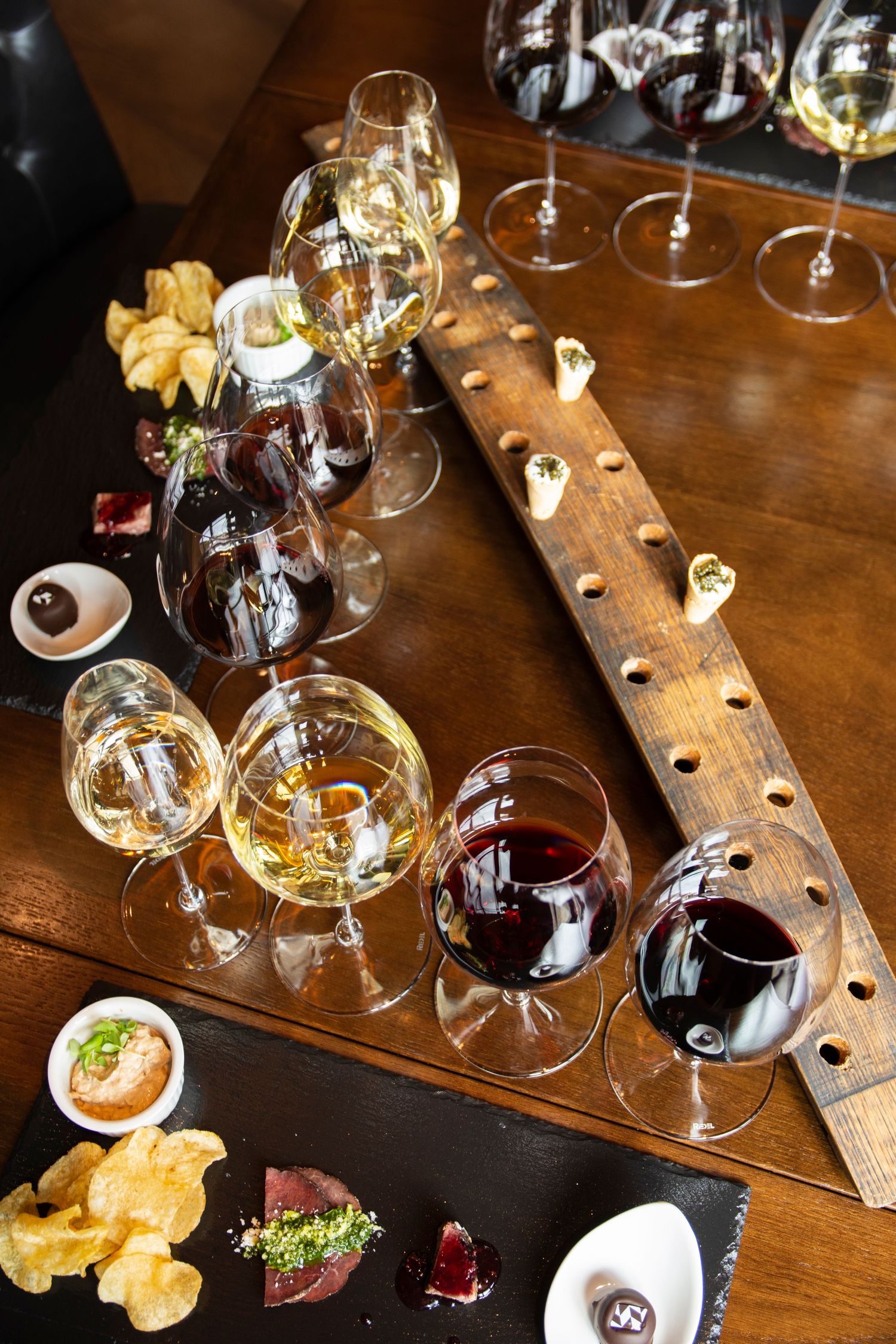 Wine tasting setup with multiple glasses and appetizers on a rustic wooden board.