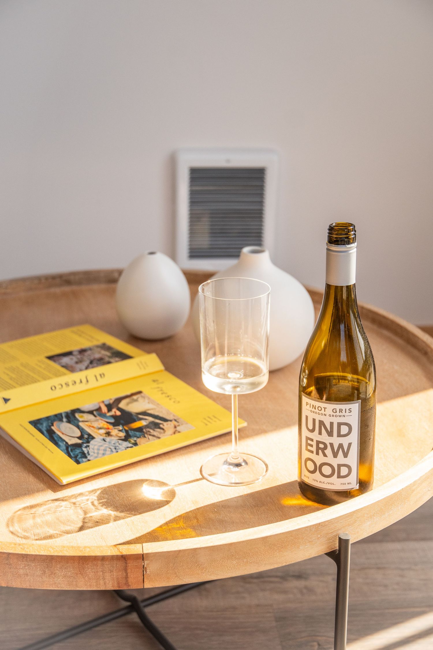 Wooden table setting with wine bottle, glasses, and yellow book in modern interior.