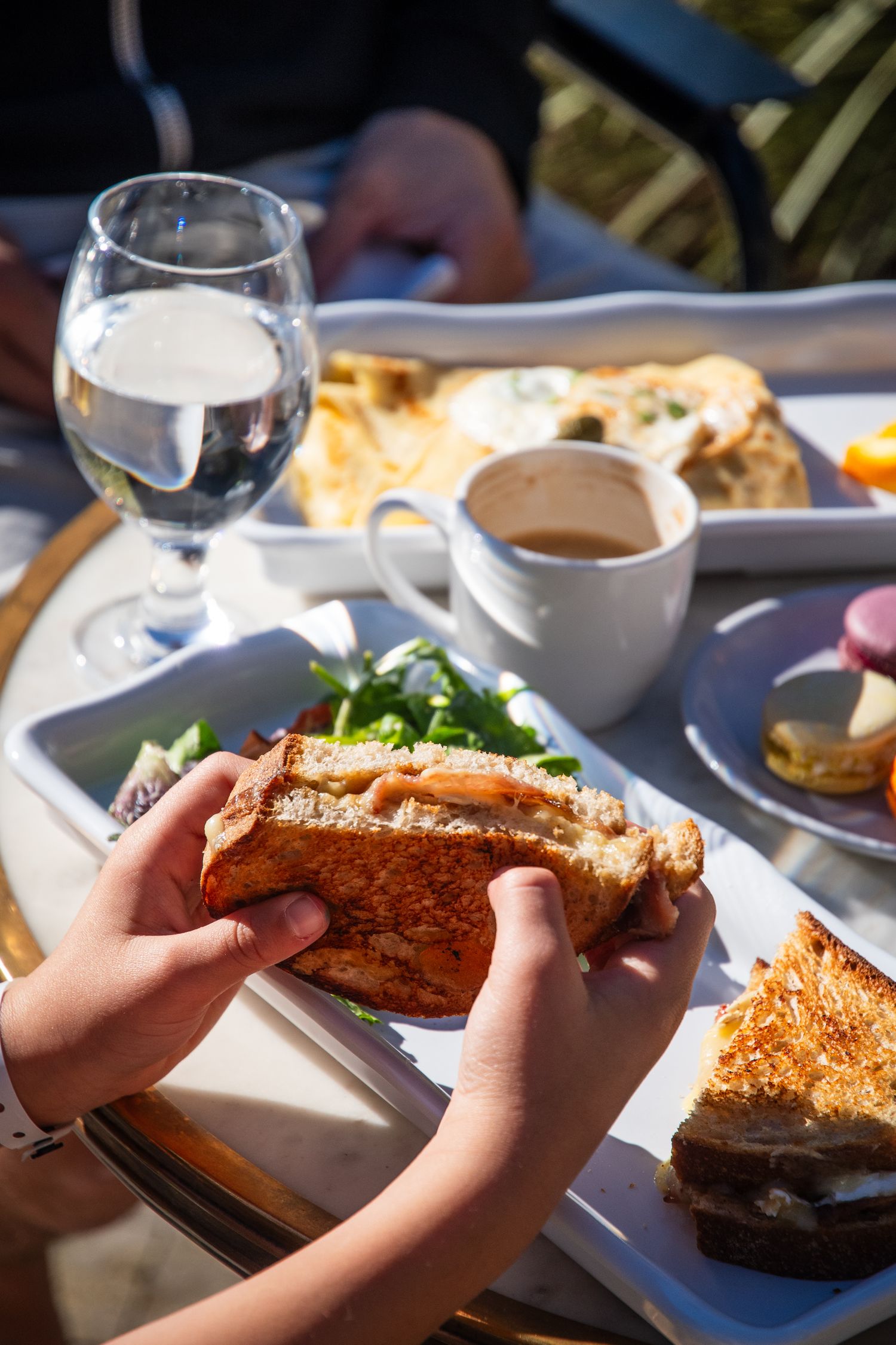 Hands breaking bread over a table set with wine glasses and plates.
