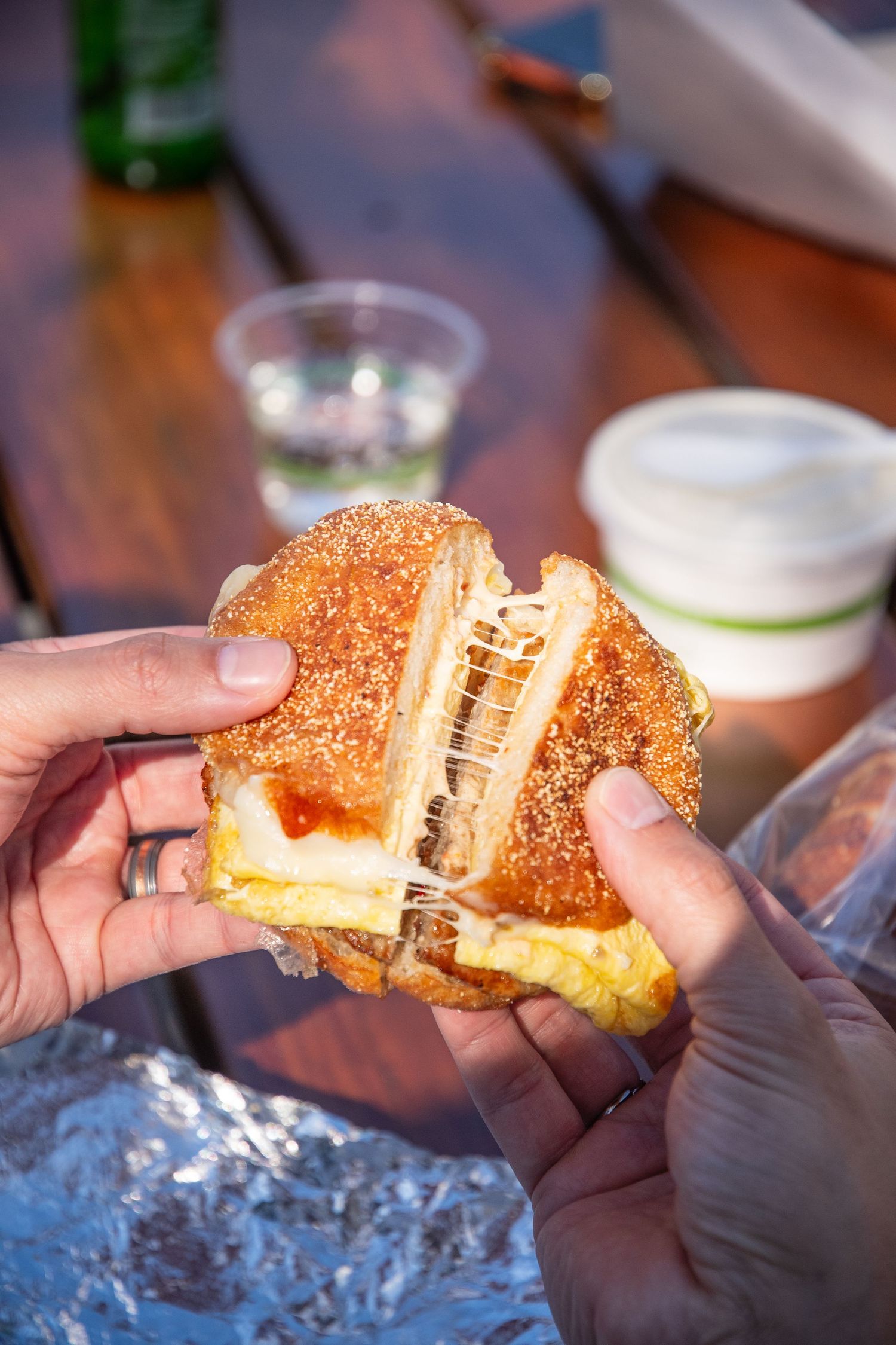 Hands pulling apart a grilled cheese sandwich on sesame bread revealing melted cheese stretch.