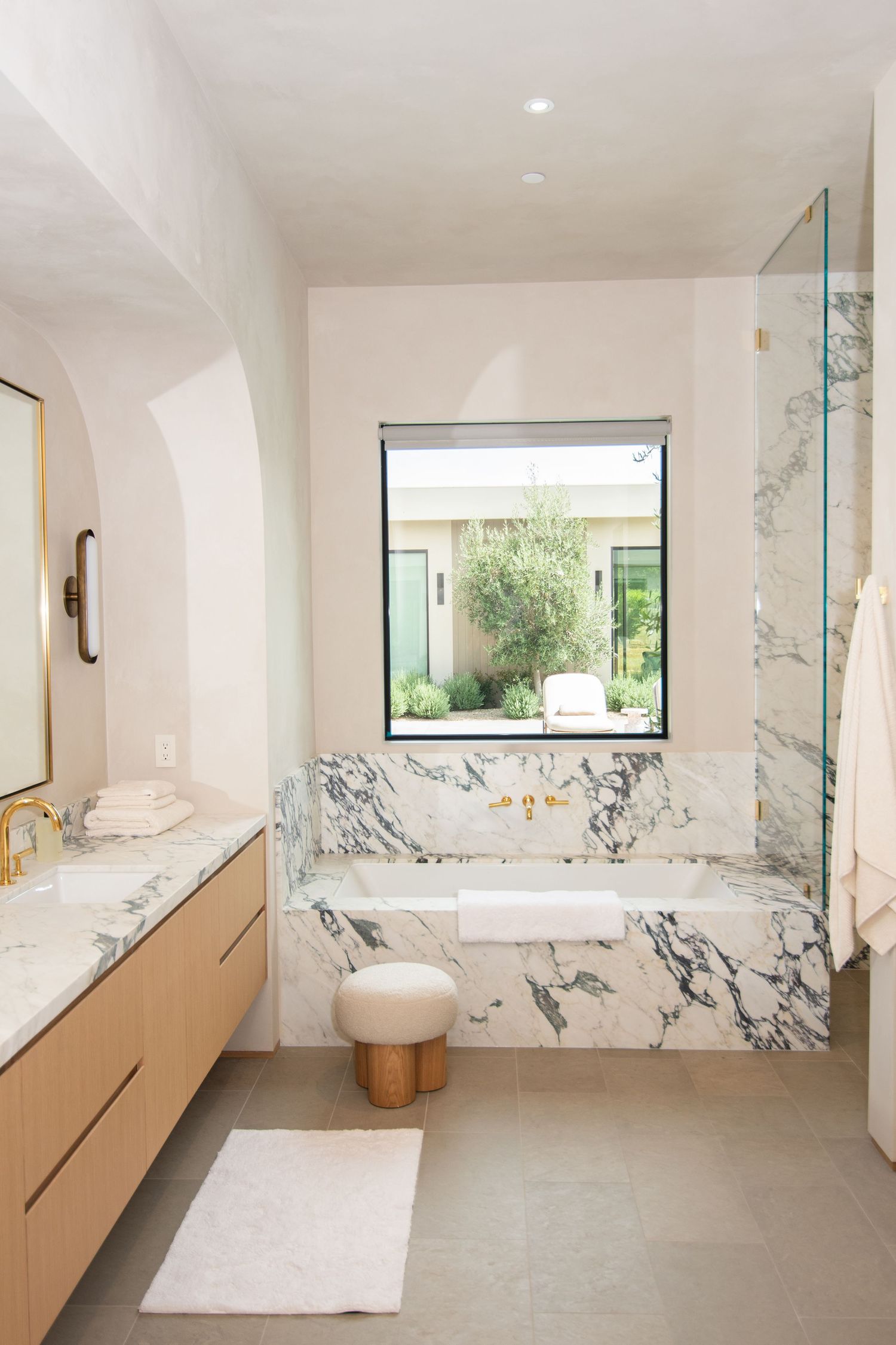 Luxurious marble bathroom with floating vanity and large window overlooking garden.