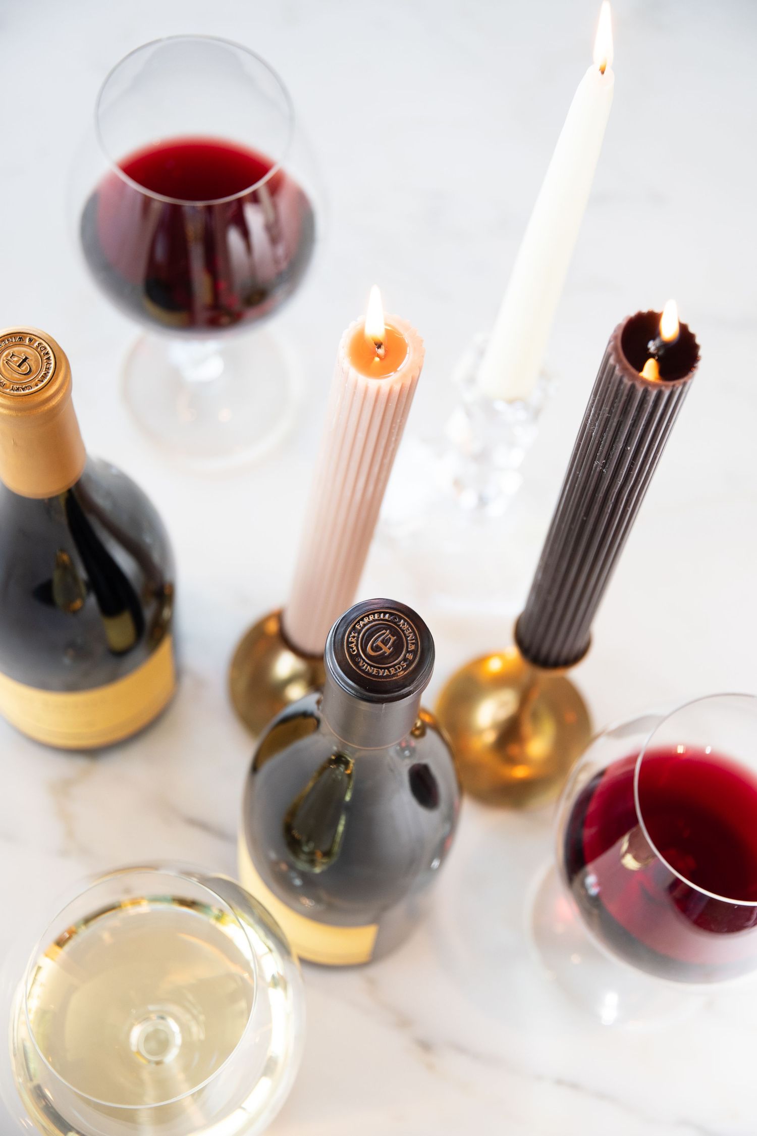 Elegant wine glasses and candles arranged on a white marble surface with red and white wine.