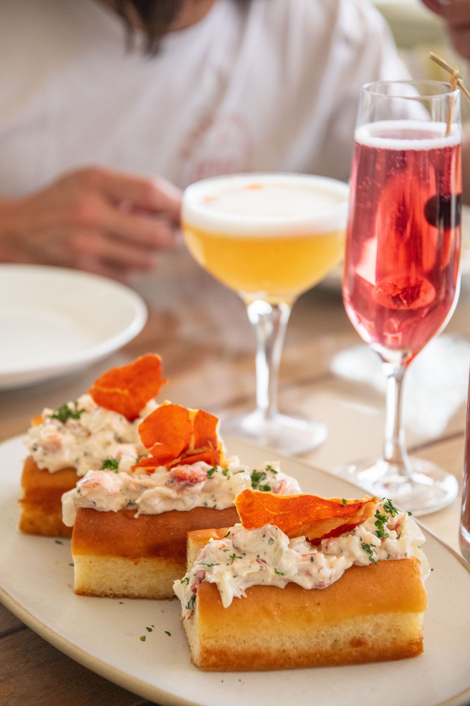 Lobster rolls garnished with fresh herbs served with rosé wine in elegant glasses.