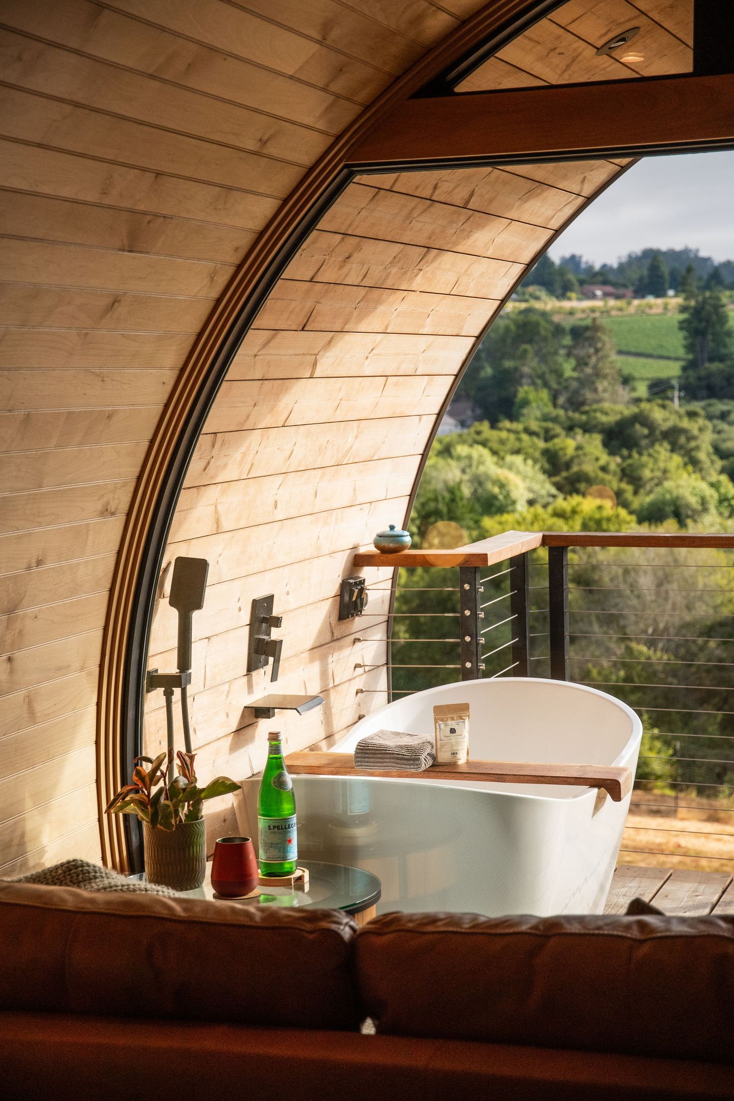 Interior view of curved wooden pod showing bathtub and scenic valley view through window.