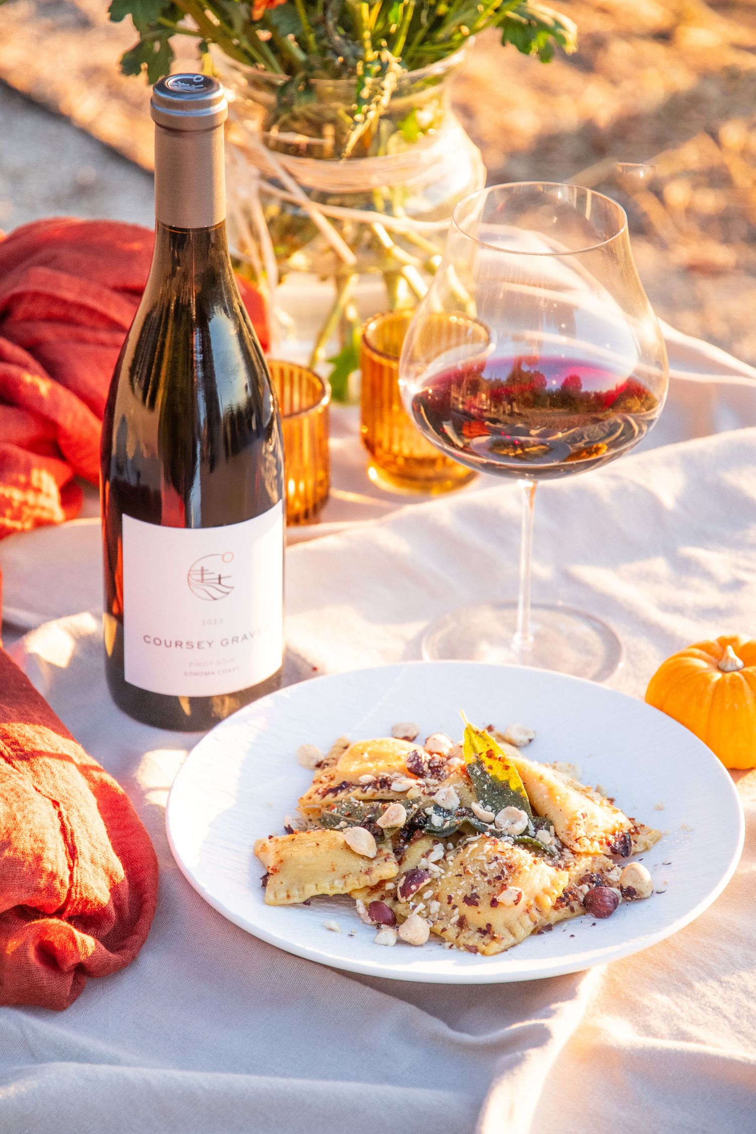 Sunlit outdoor dining scene with wine bottles and plated dishes on white linens.