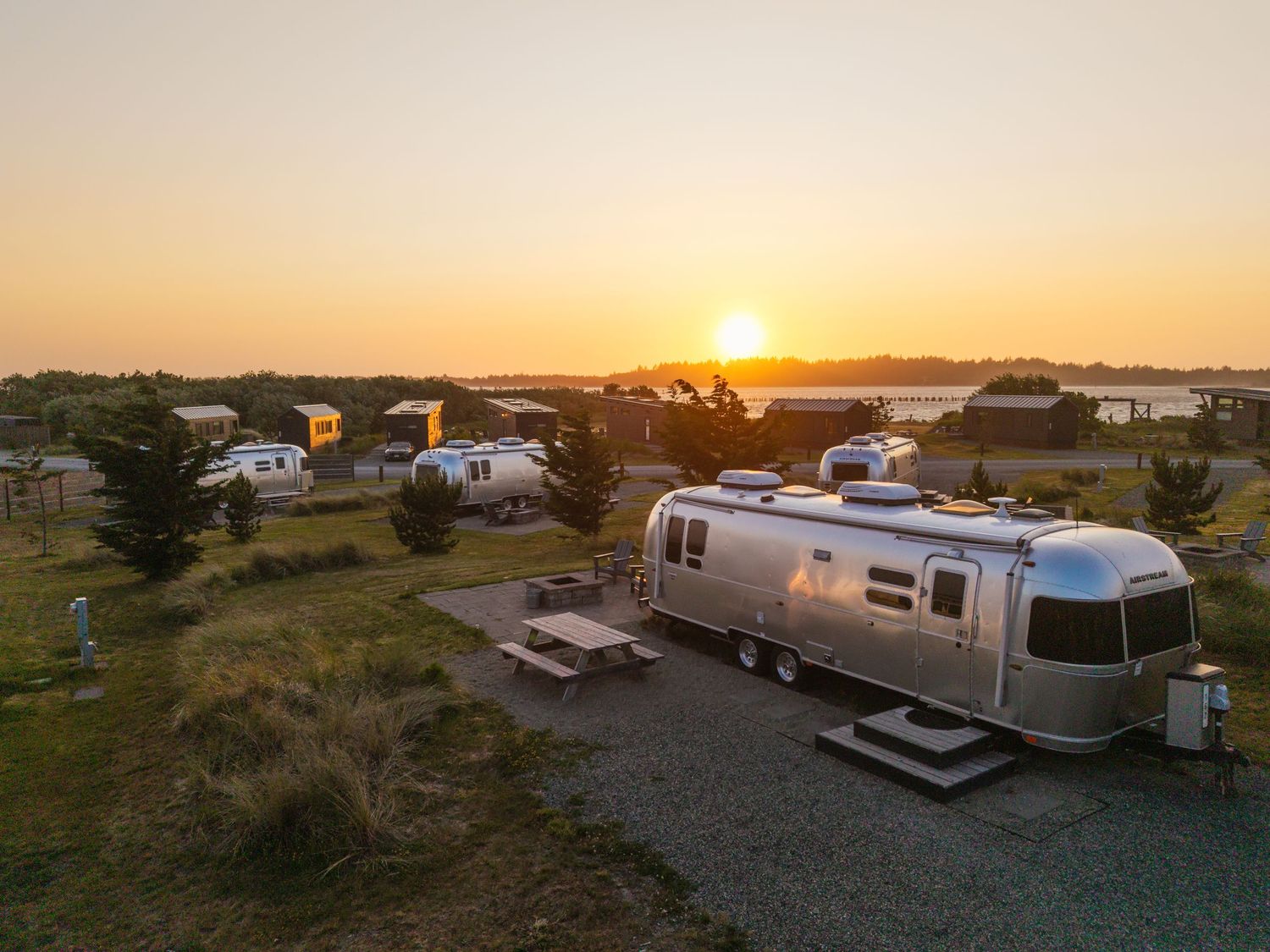Airstream trailers parked at a scenic coastal campground during a golden sunset over calm waters.