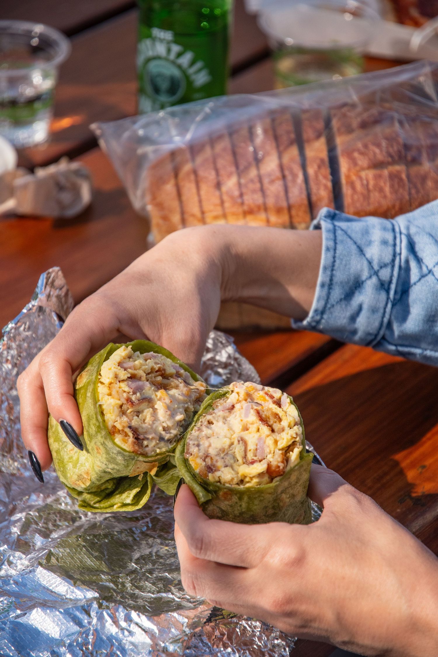 Hands holding an unwrapped lettuce wrap sandwich with sliced bread visible on wooden table.