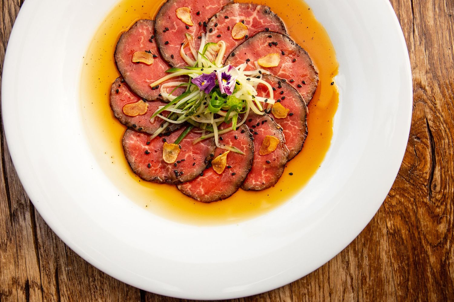 Plated beef carpaccio with garnish served on white plates against a wooden table surface.