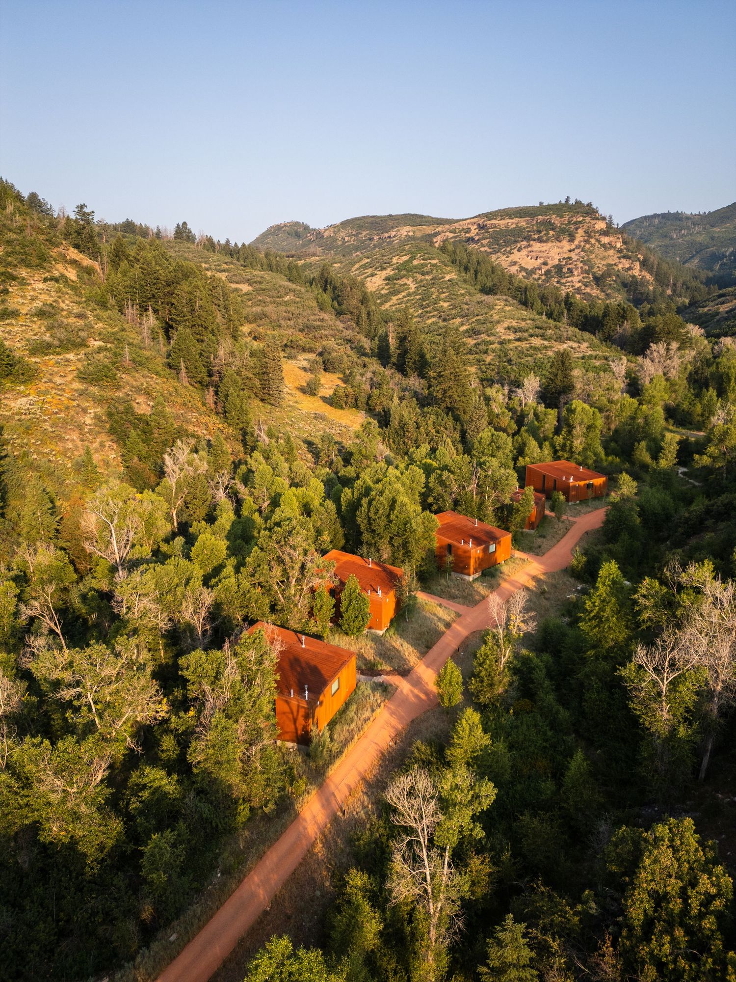Aerial view of winding red dirt road through green mountain landscape.