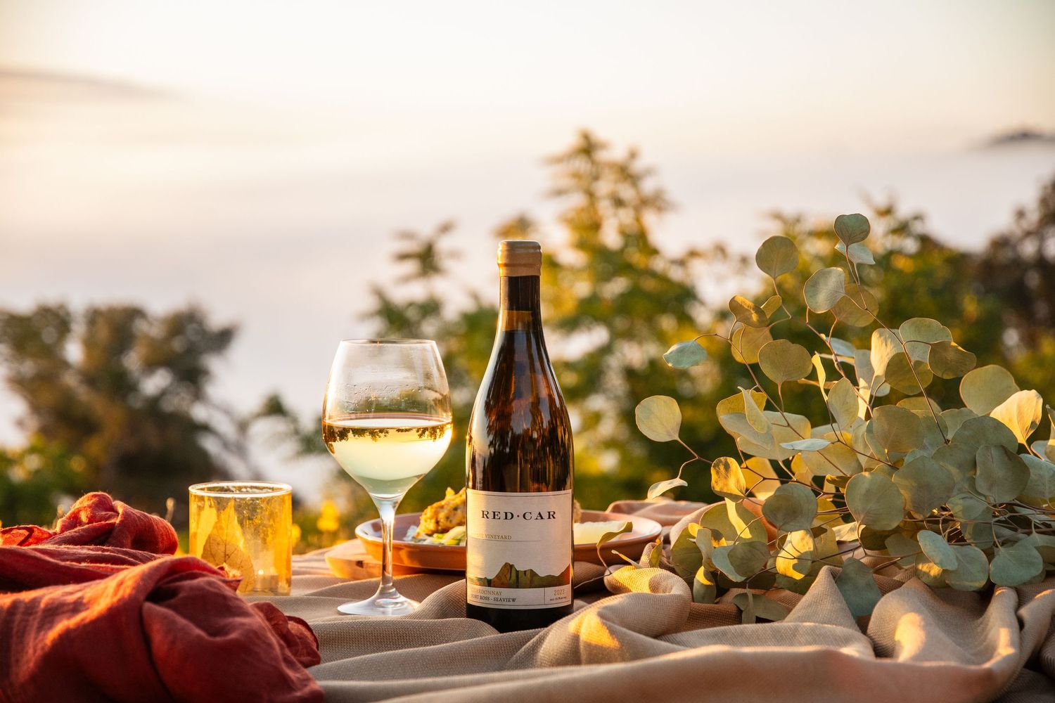 Romantic outdoor wine tasting setup with bokeh lights and eucalyptus leaf decorations.