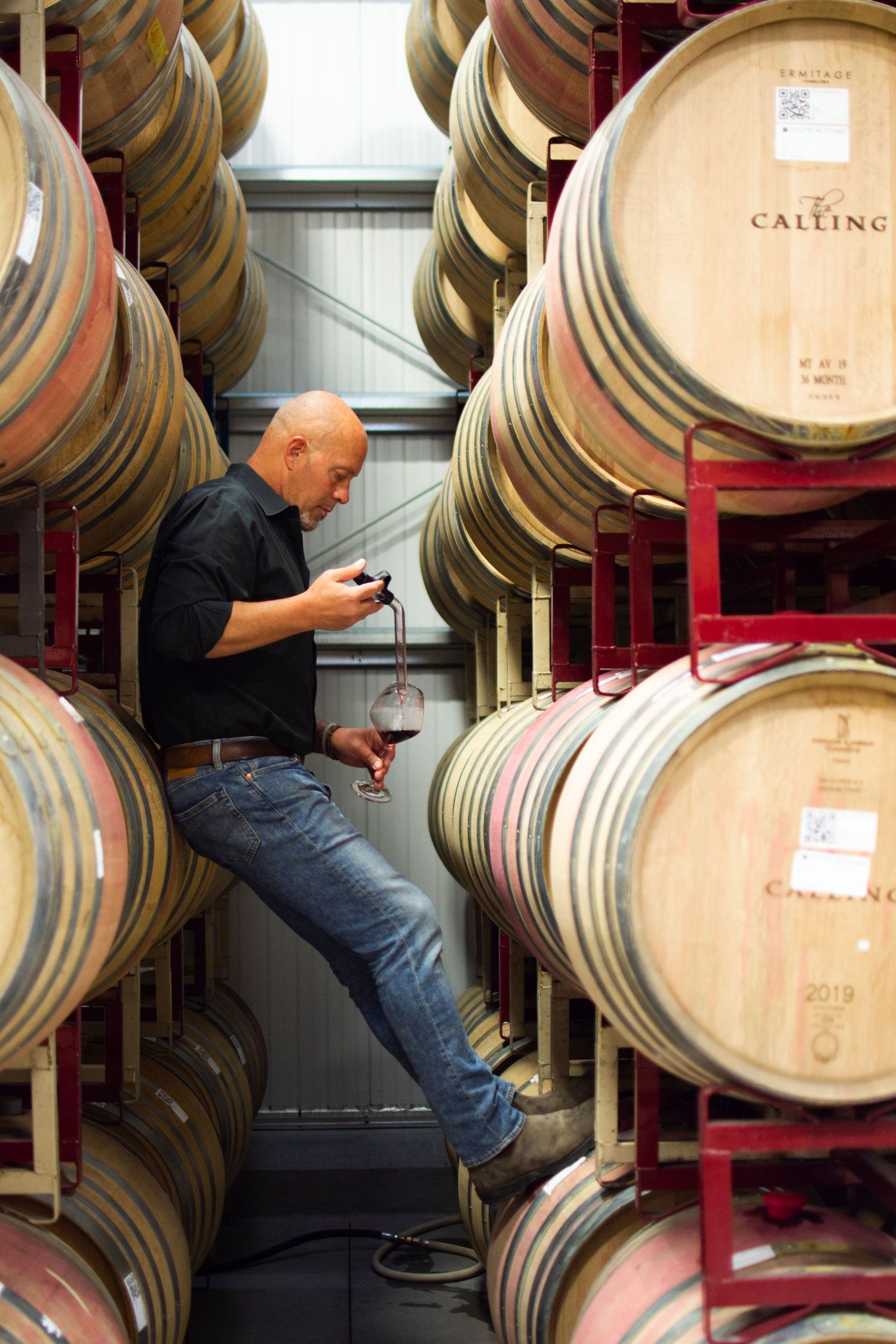 Wine barrels stacked in cellar with worker checking quality and maintenance.