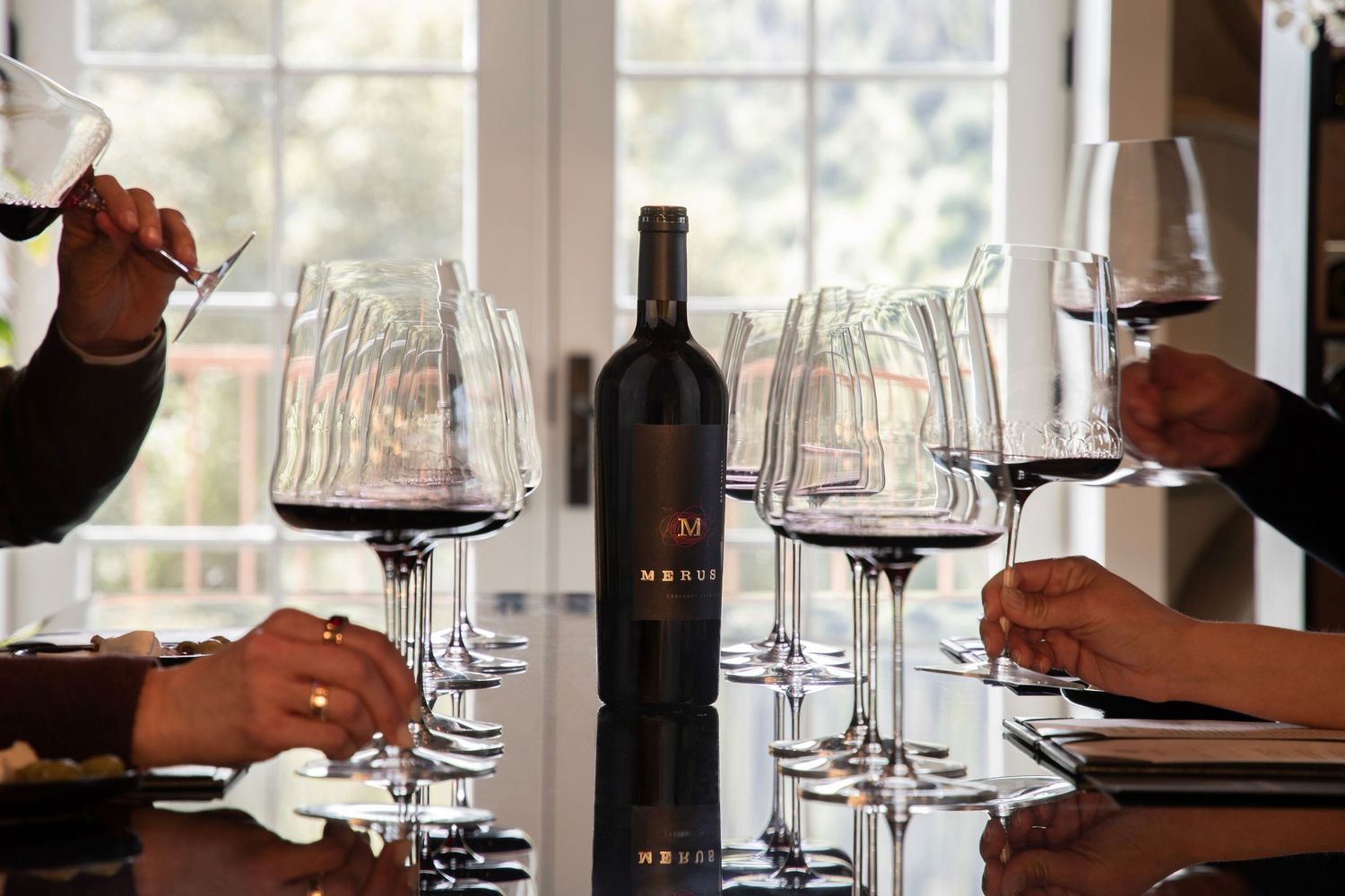 Group of people tasting Merva red wine from large glasses around a table during a winery tasting session.