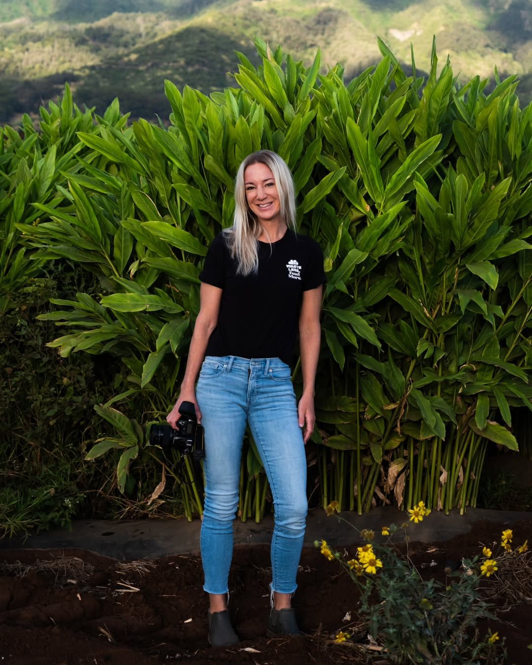 A casual portrait in front of lush tropical plants and mountain scenery.
