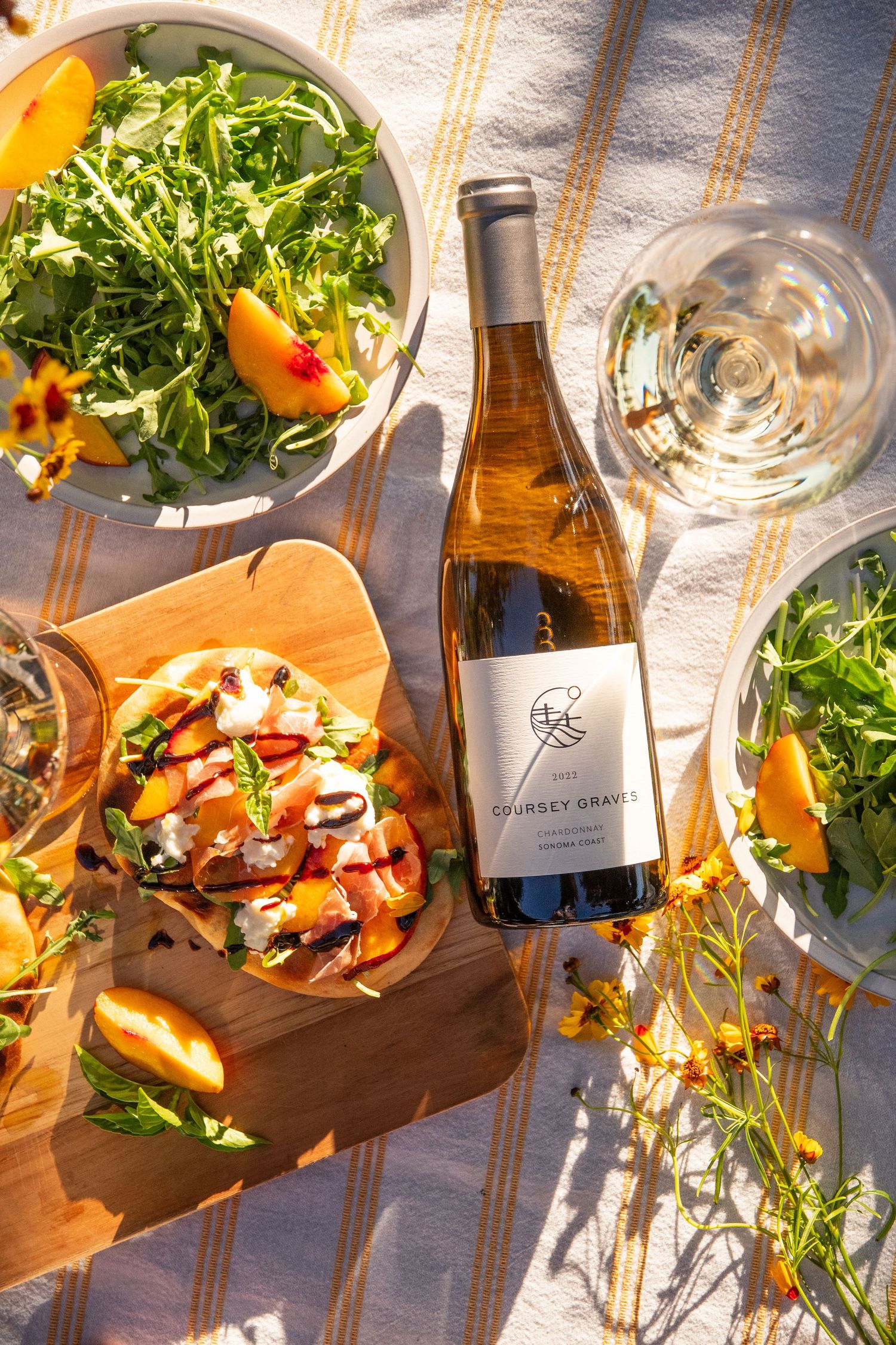 Overhead view of wine bottle, salad, and appetizers on striped picnic blanket.