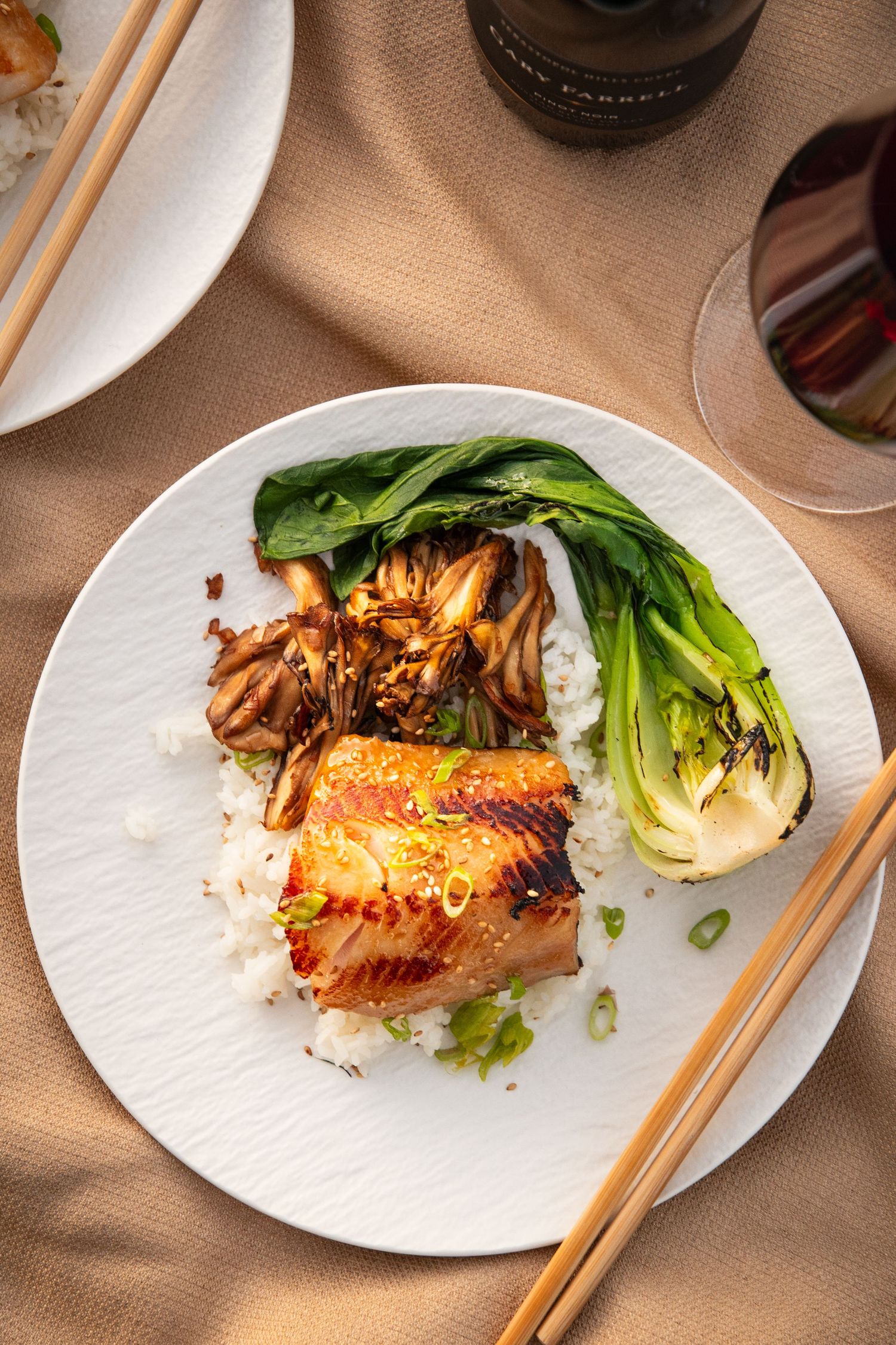 Grilled salmon with Asian glaze and bok choy served on white plates with wooden chopsticks.