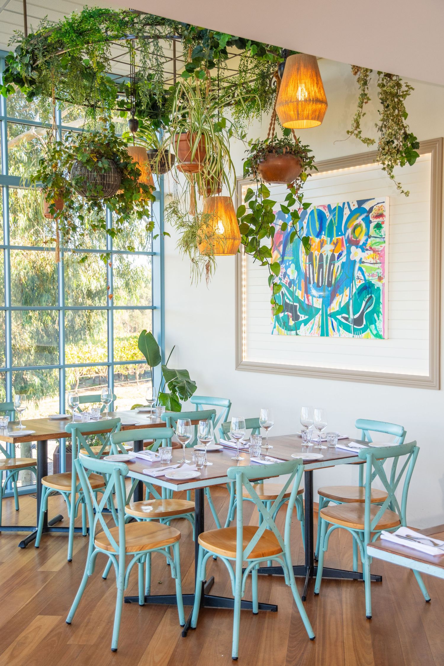 Bright restaurant interior with mint green chairs, hanging plants, and modern coastal decor.