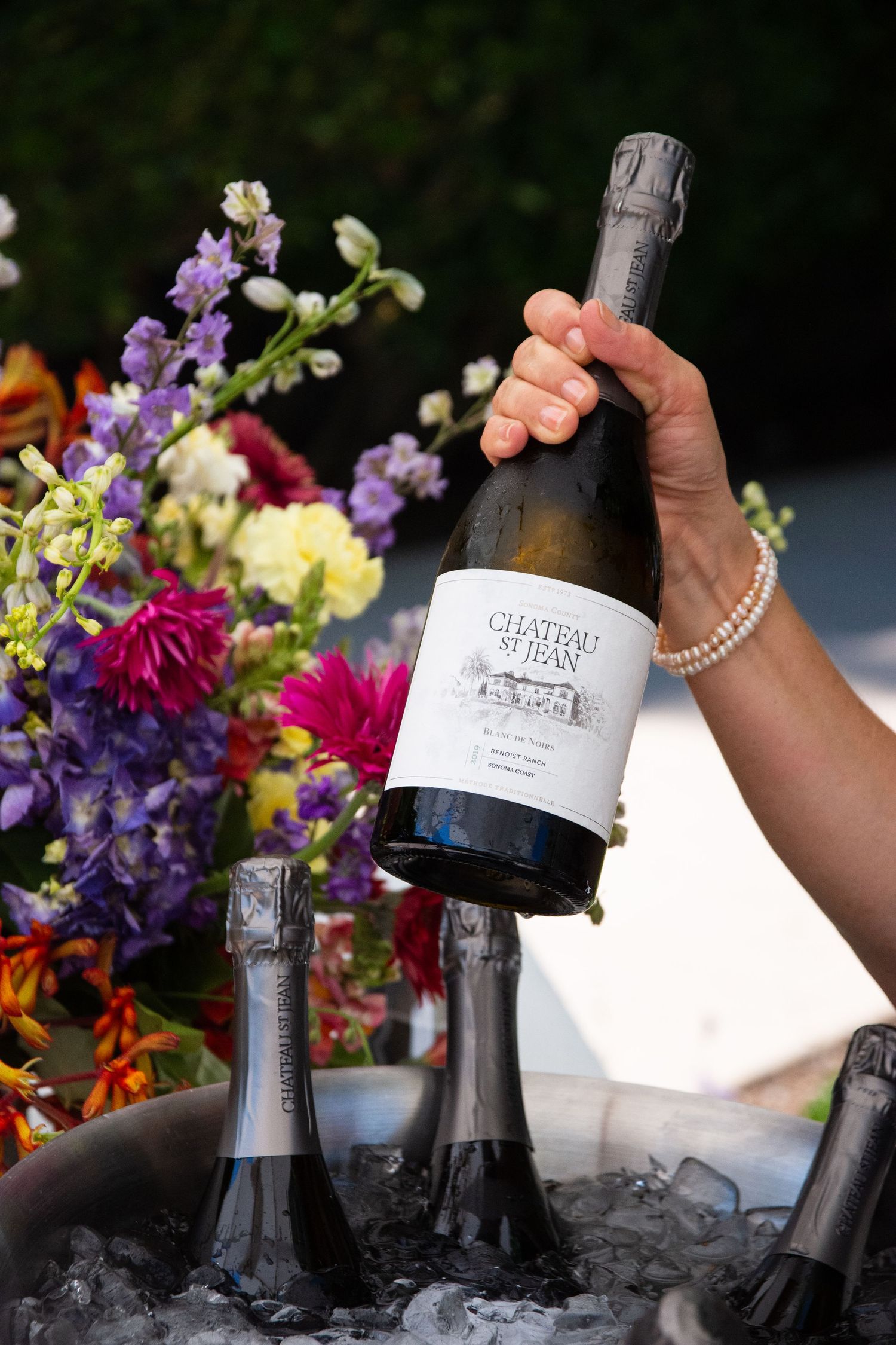 Champagne bottles on ice surrounded by colorful floral arrangements at an event.