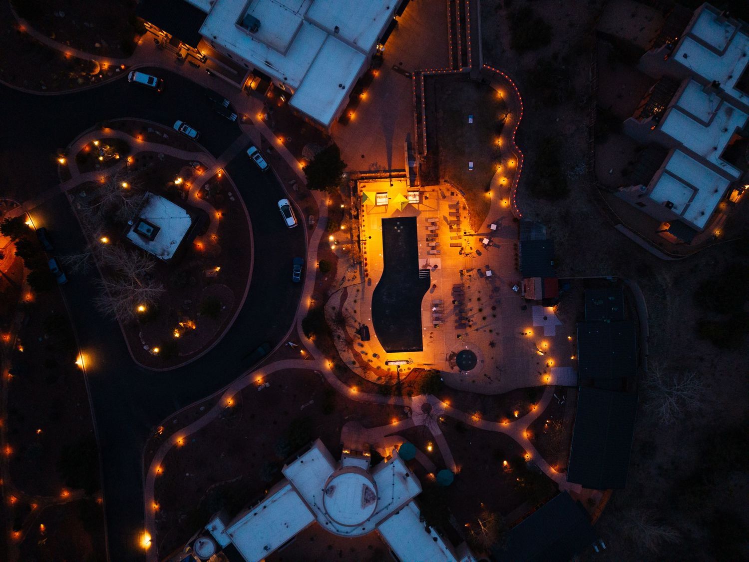Bird's eye aerial view of a resort complex at night with glowing orange lights tracing circular driveways.