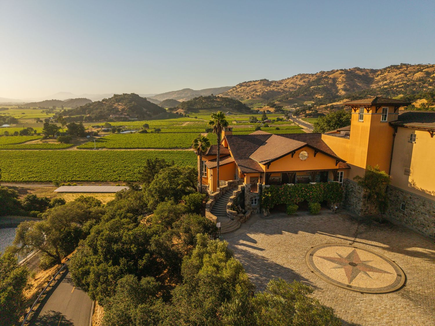 Aerial view of a scenic winery estate with vineyards, rolling hills, and a compass rose courtyard at golden hour.