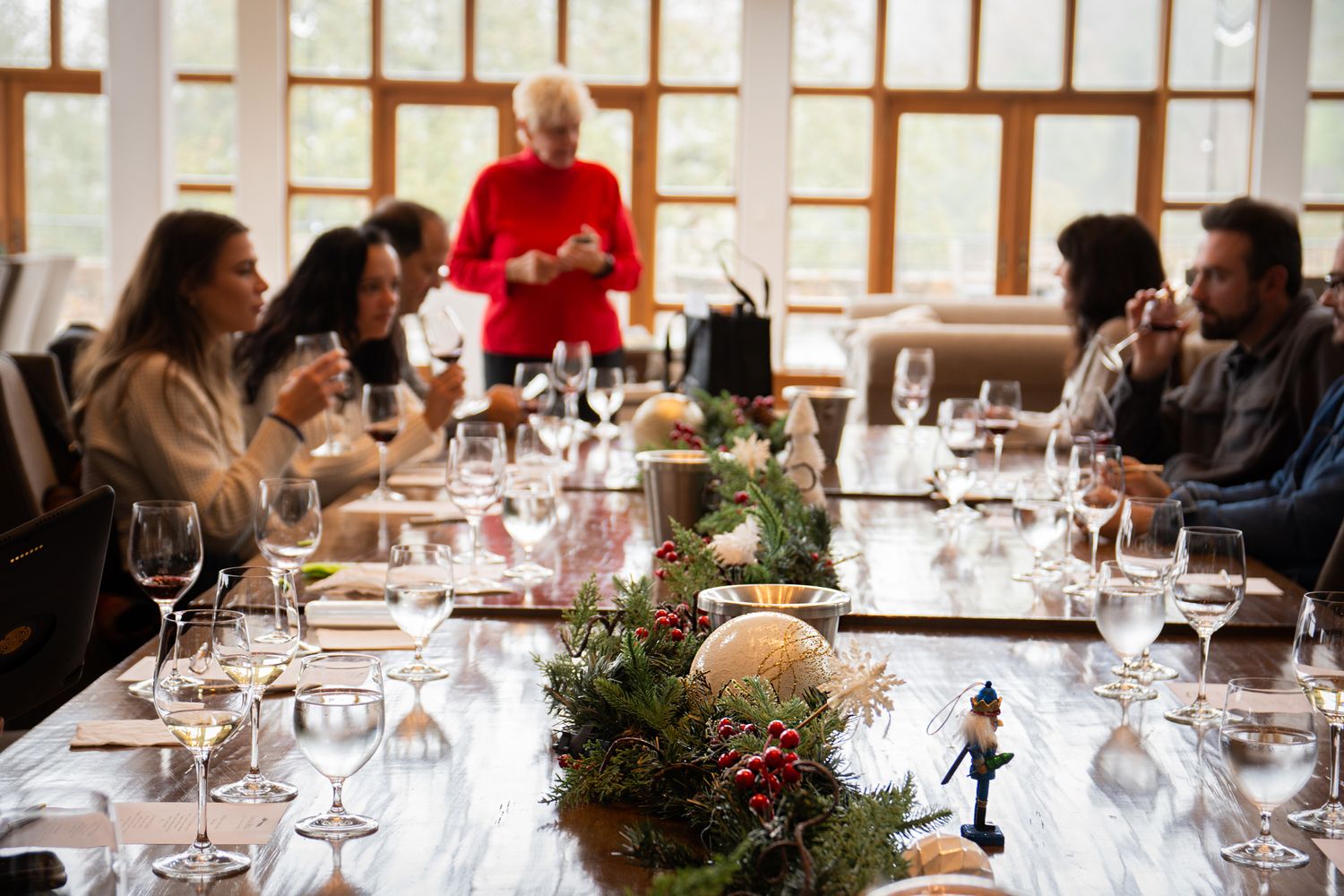 Holiday wine tasting event with decorated table featuring evergreen centerpiece and glassware.