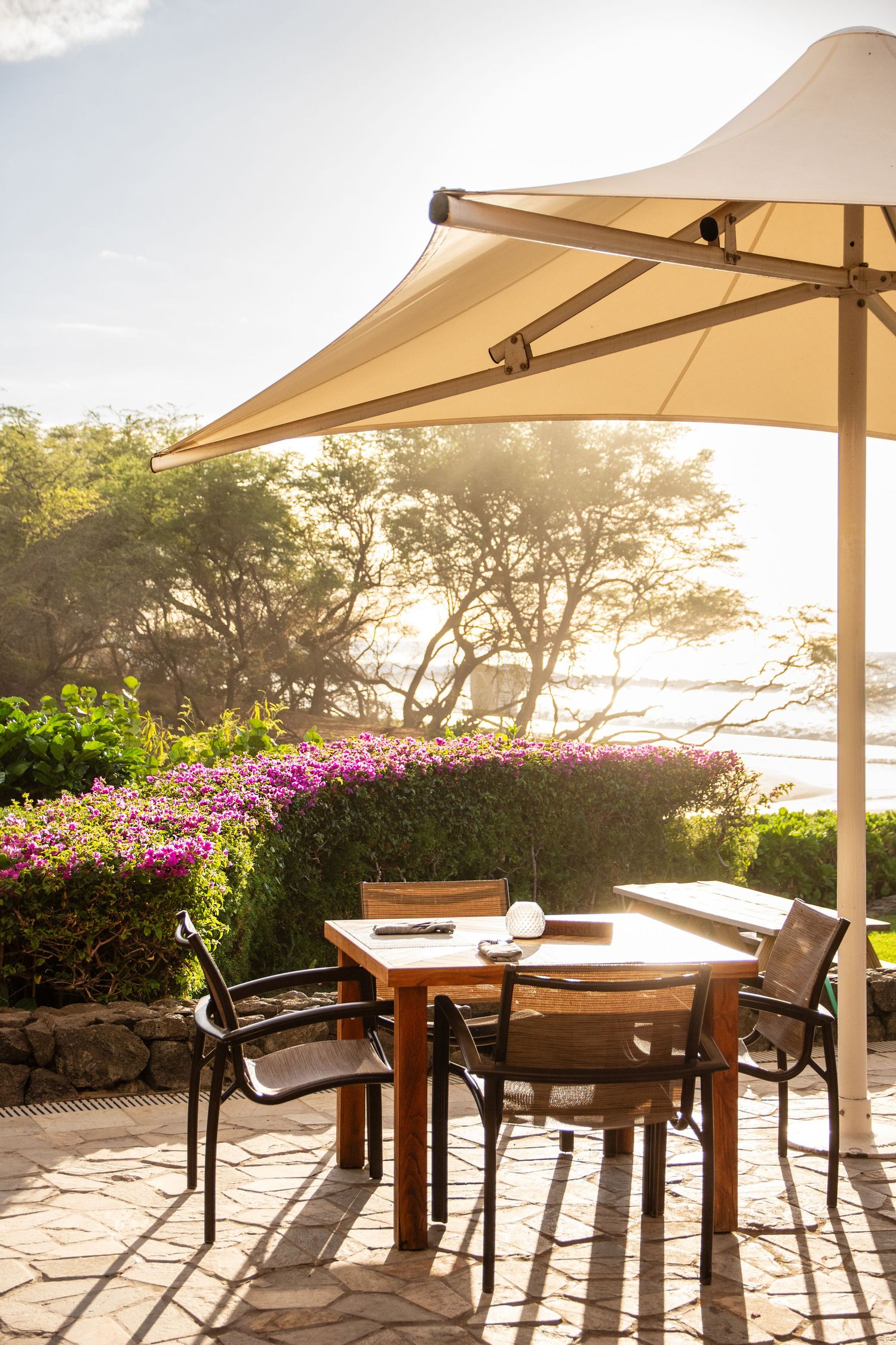 Outdoor dining tables with umbrellas overlooking a scenic ocean view at sunset.