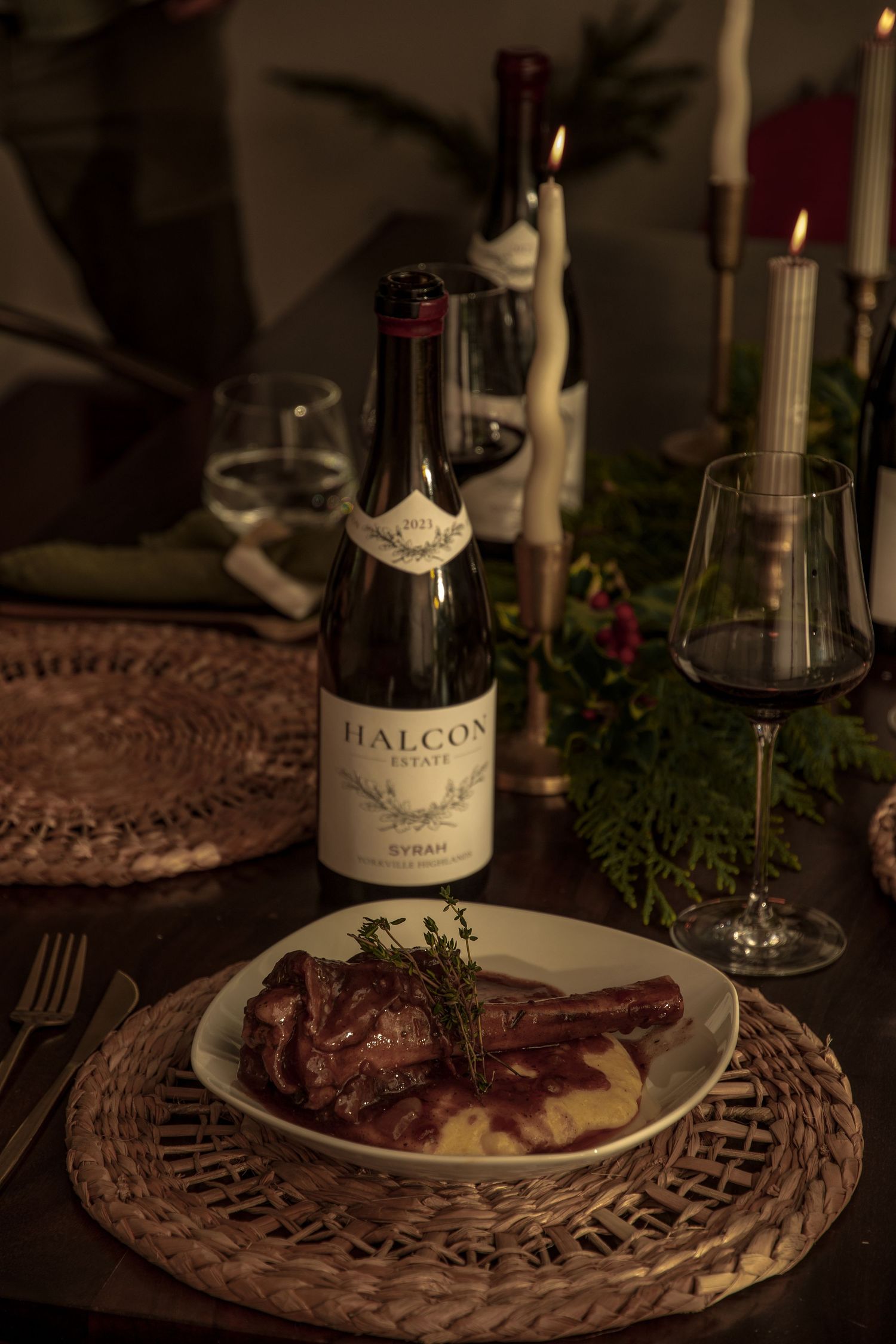 Elegant dinner setting with a bottle of Halcon wine, meat dish on woven placemat, and candlelight creating ambiance.