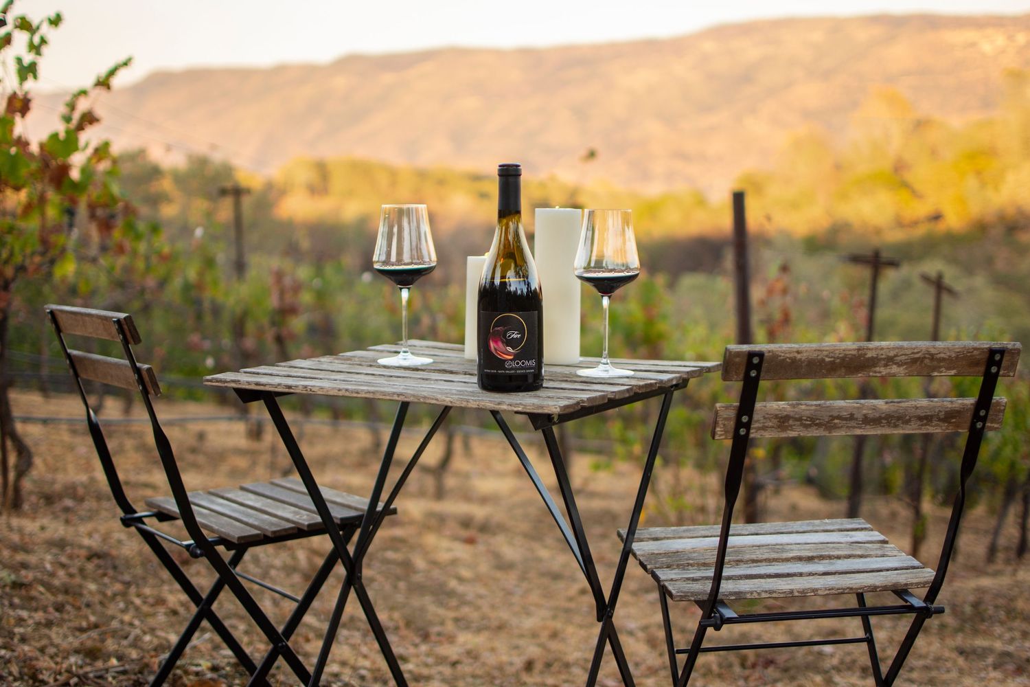 Outdoor seating area with bistro tables and chairs overlooking vineyard at sunset.