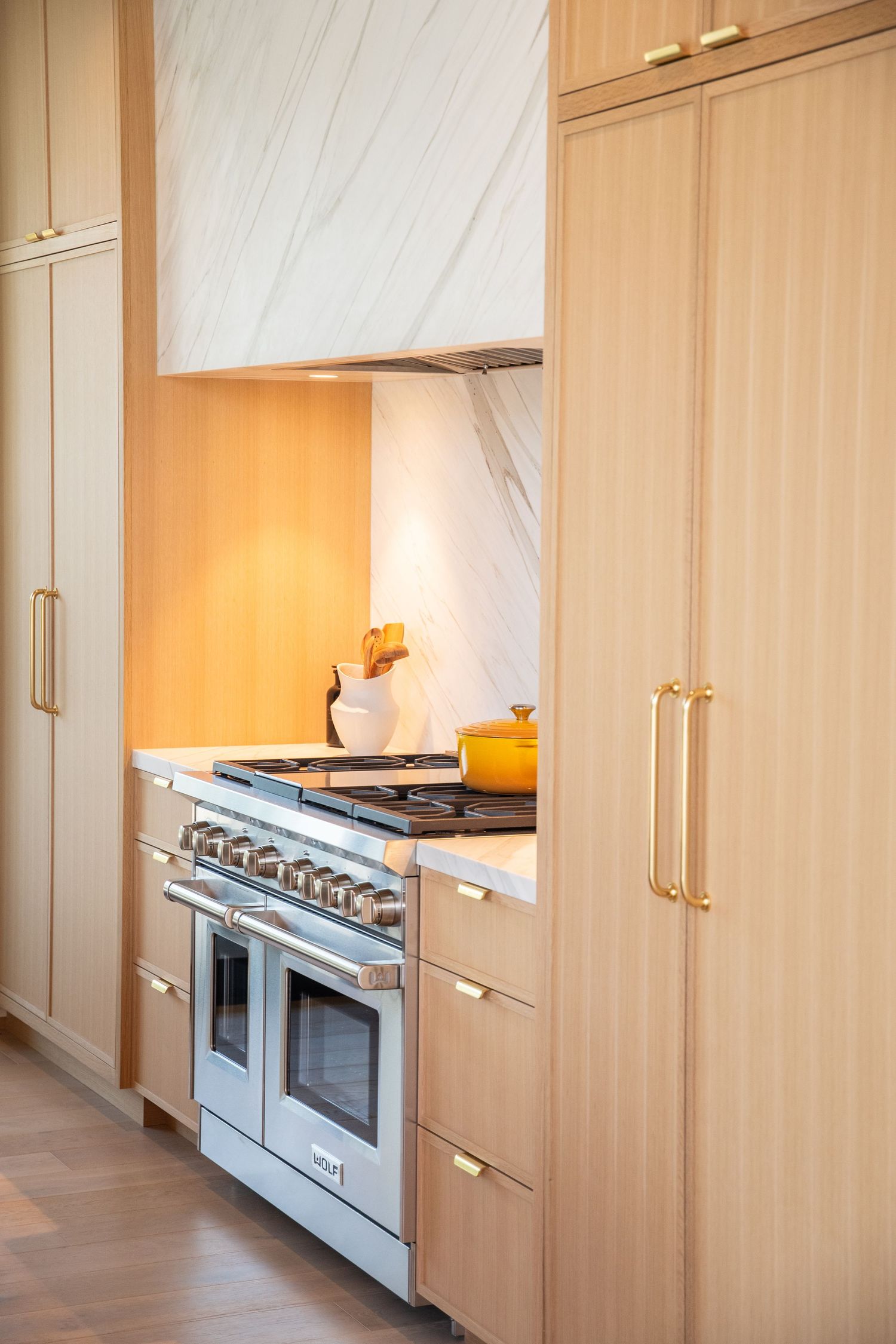 Modern kitchen with light wood cabinets and professional gas range under marble hood.
