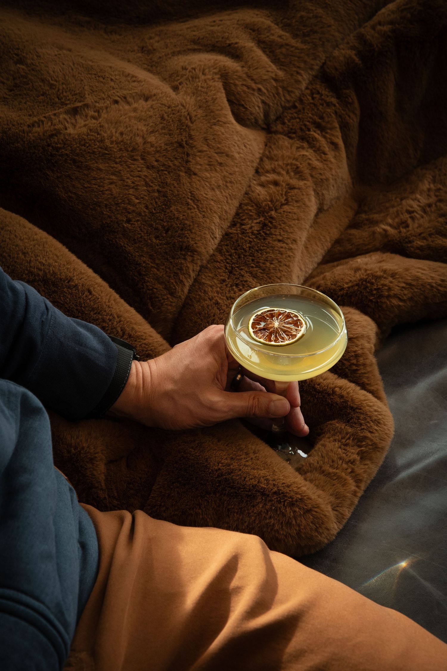 Citrus garnished cocktail being held against a brown textured background.