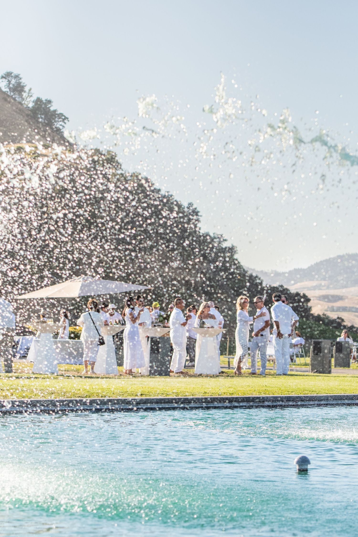 Group in white clothing creates splash by pool with mountains in background.