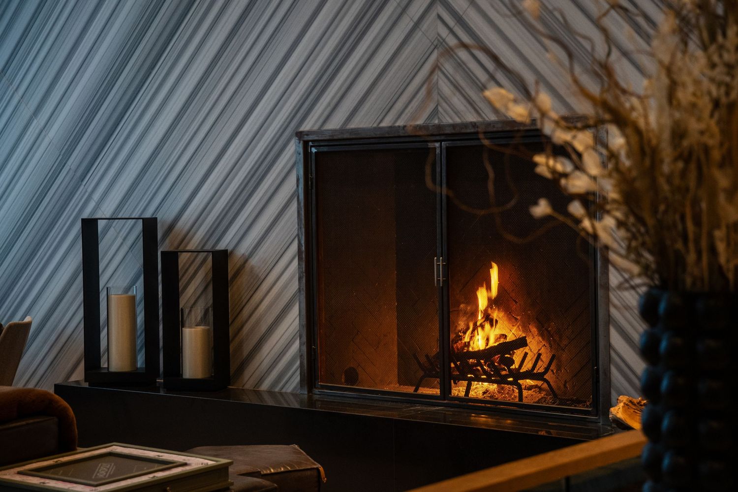 Modern fireplace with burning logs and glass lanterns creating cozy ambiance.