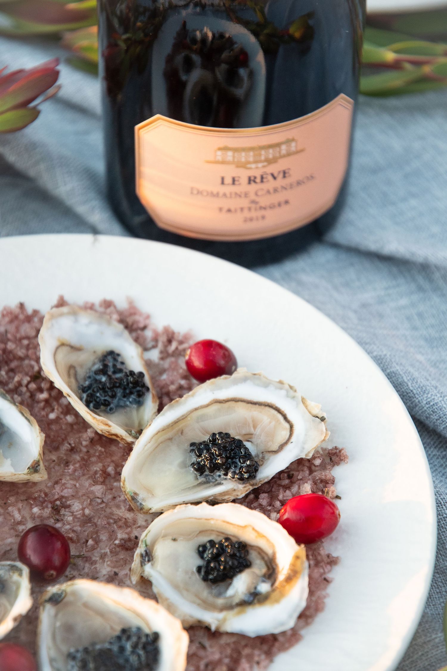 Elegant plating of oysters with caviar and champagne bottles in the background.